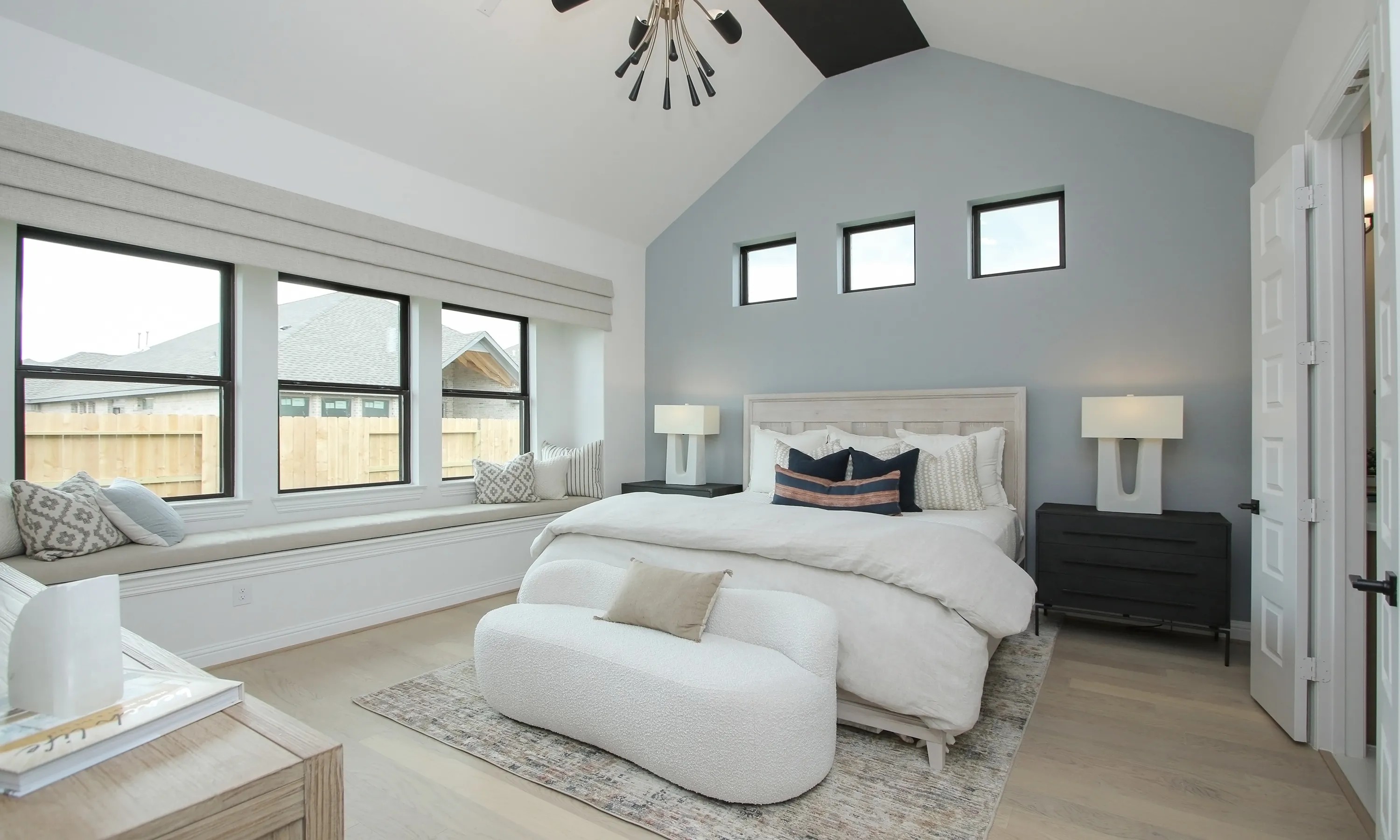 Modern bedroom with vaulted ceiling, elegant lighting, large windows in Coastal Point. Stylish decor enhances luxury.