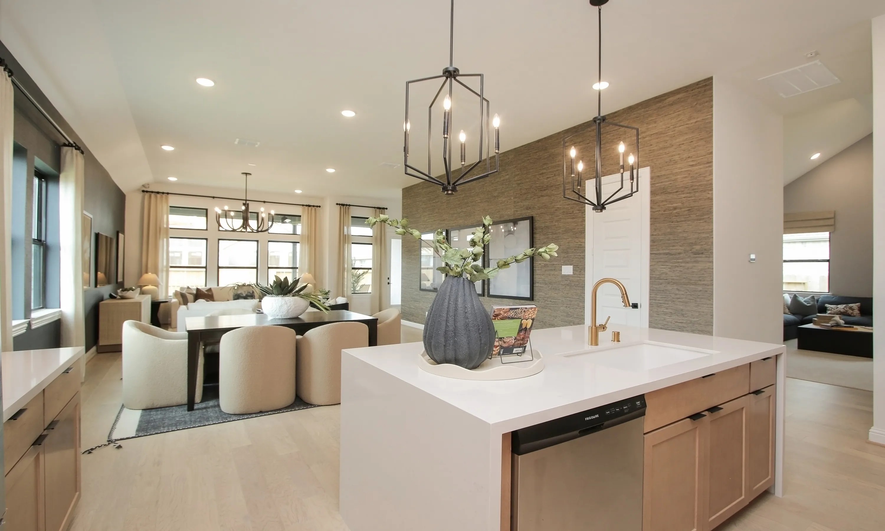 Modern kitchen and dining area featuring geometric lighting, sleek island, and beige decor in Coastal Point community.