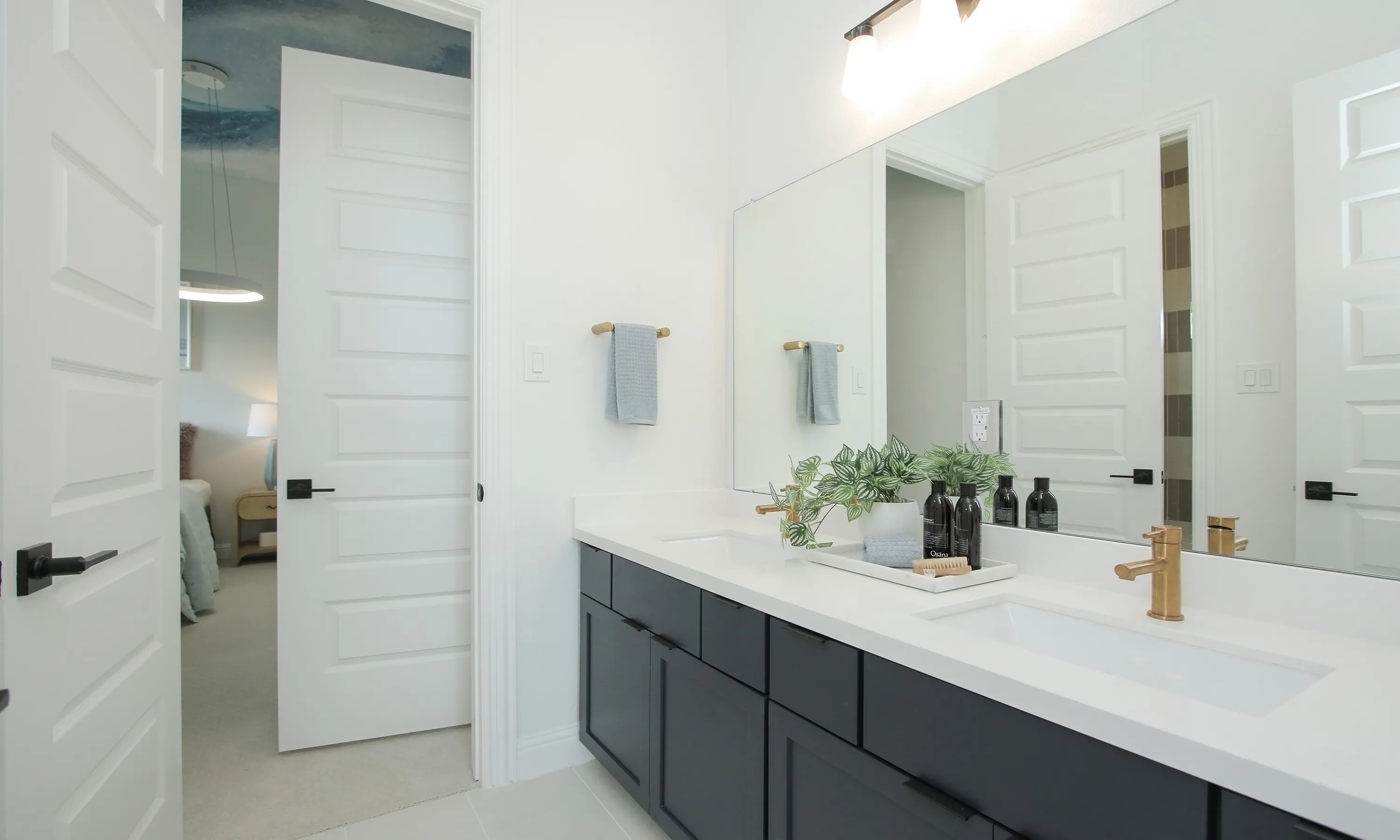 Modern bathroom with dual sinks, black cabinets, gold fixtures, large mirror, and white doors. Coastal Point community.