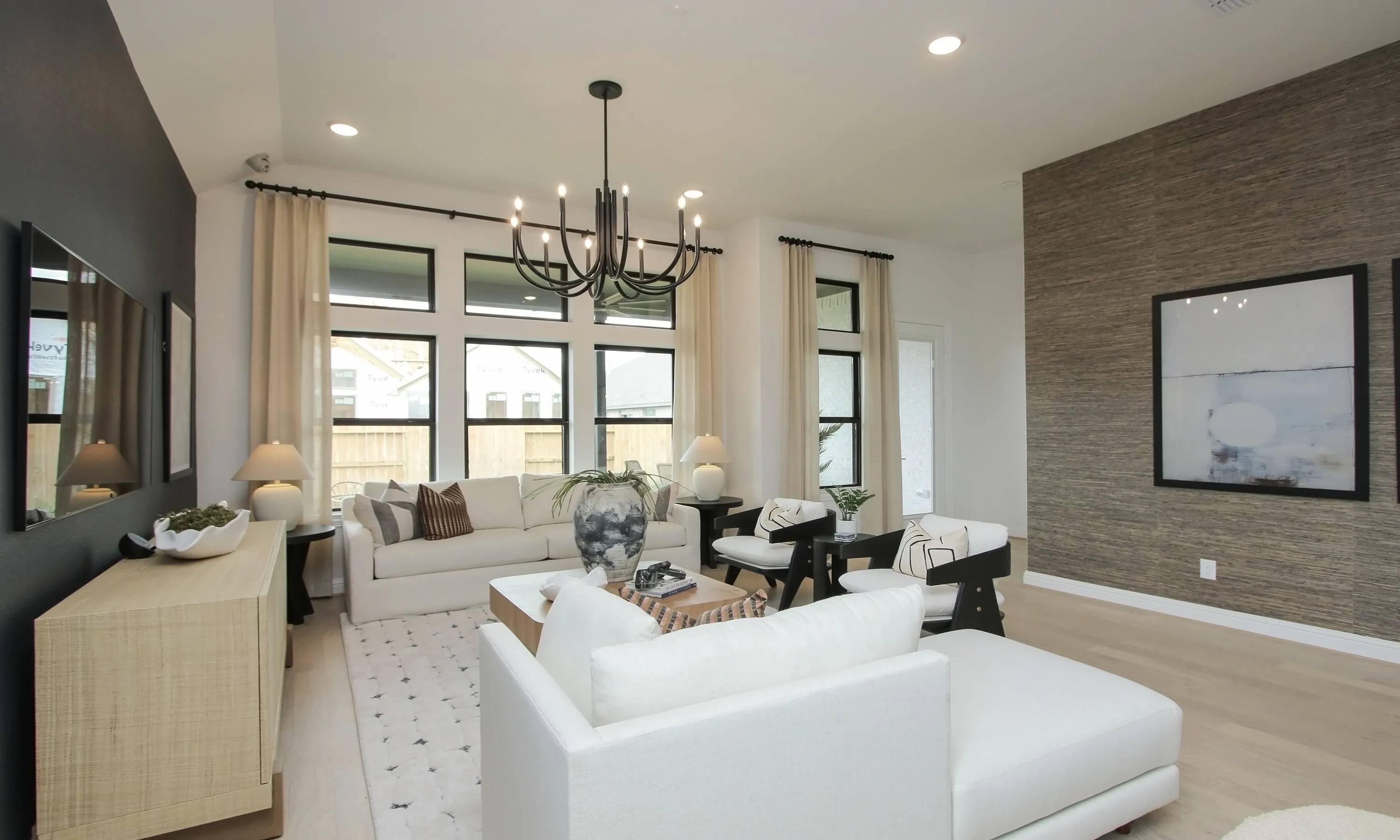 Elegant living room in Coastal Point community with modern chandelier, large windows, textured accent wall, neutral decor.