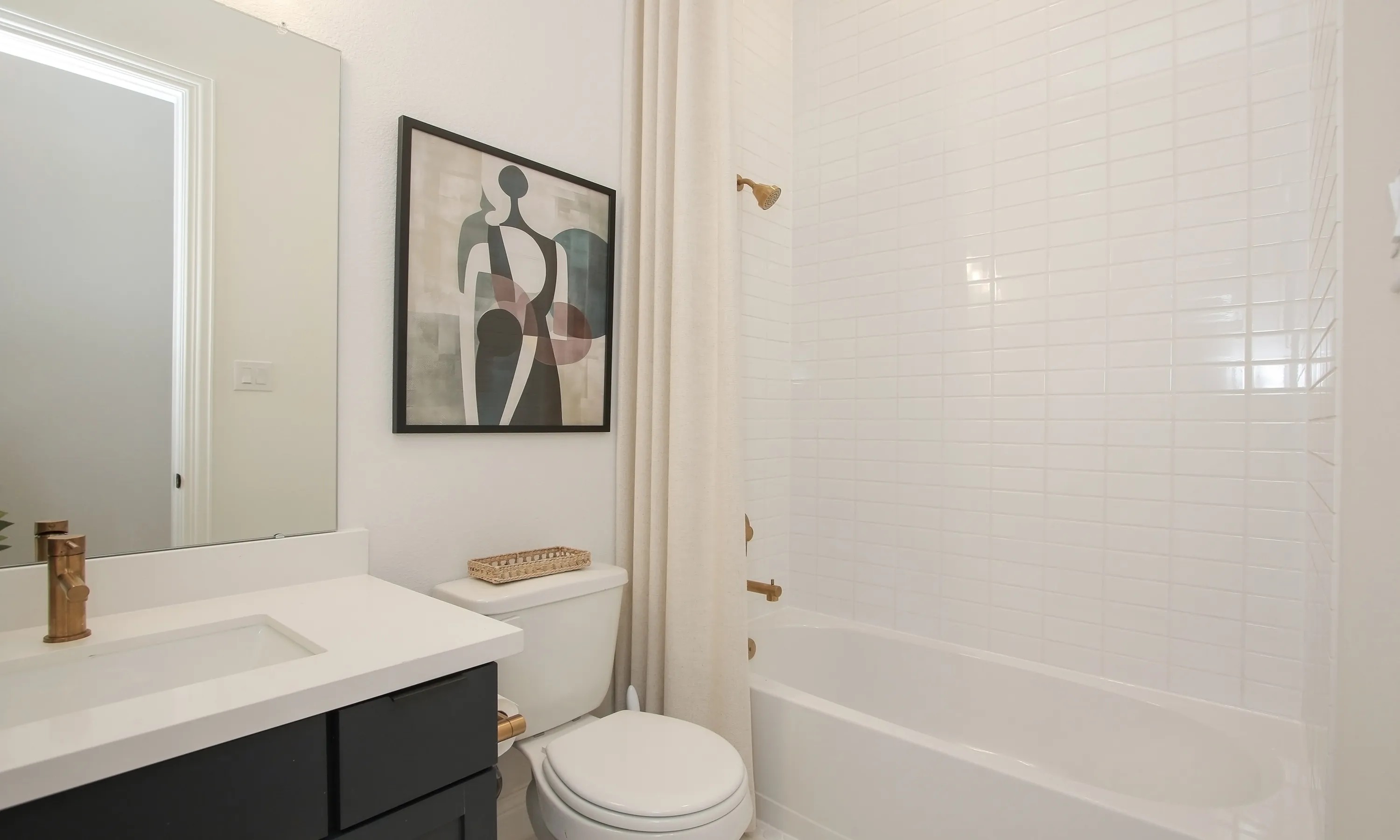 Modern bathroom with white tiles, abstract art, brass fixtures in Coastal Point community.