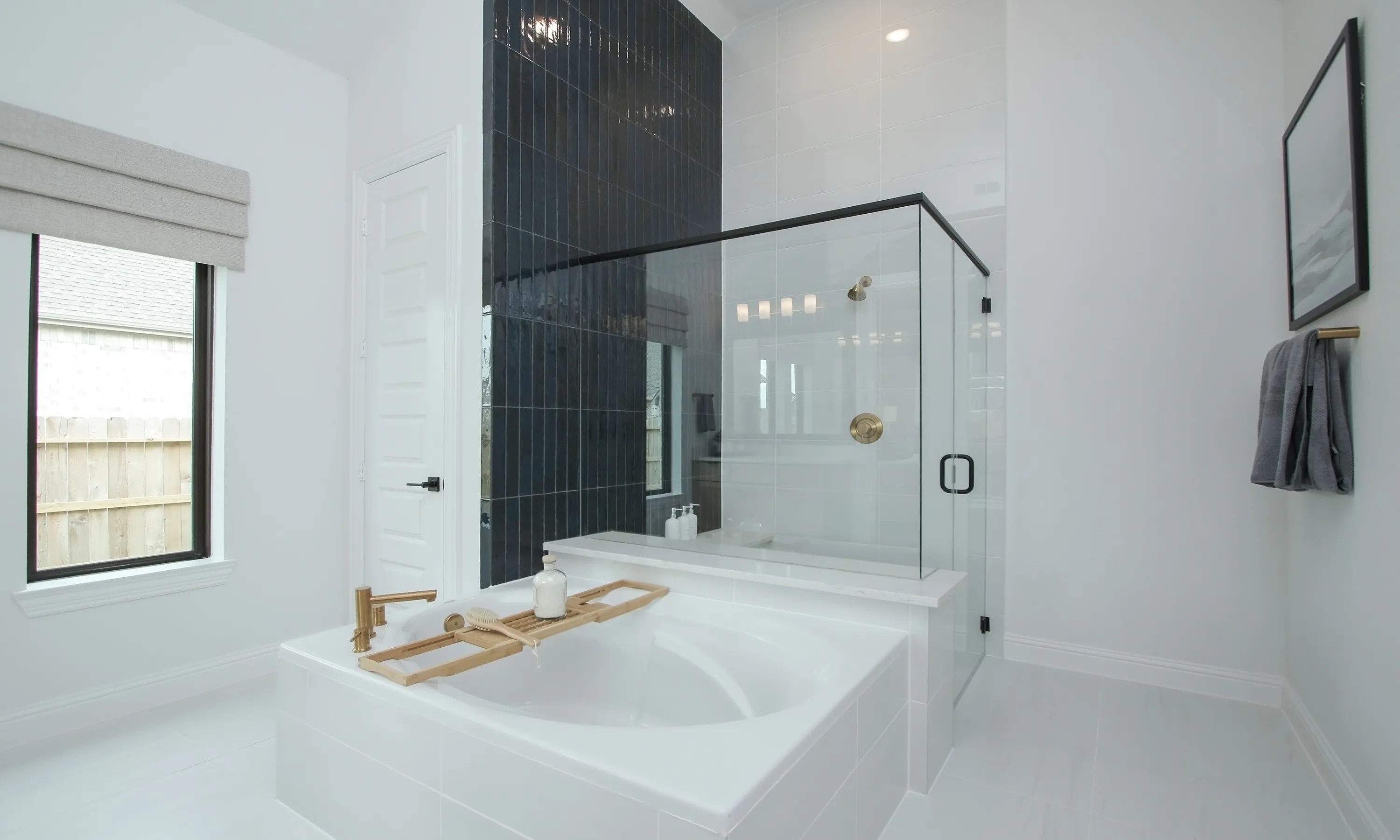 Luxurious Coastal Point bathroom with freestanding tub, gold fixtures, glass shower, and elegant black tile wall.