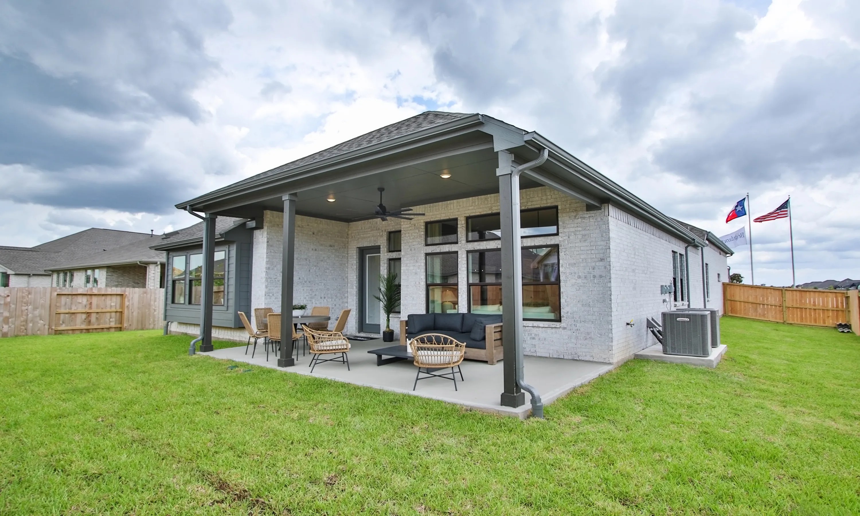 Elegant patio with ceiling fans, brick exterior, and manicured lawn in Coastal Point, Texas suburb.