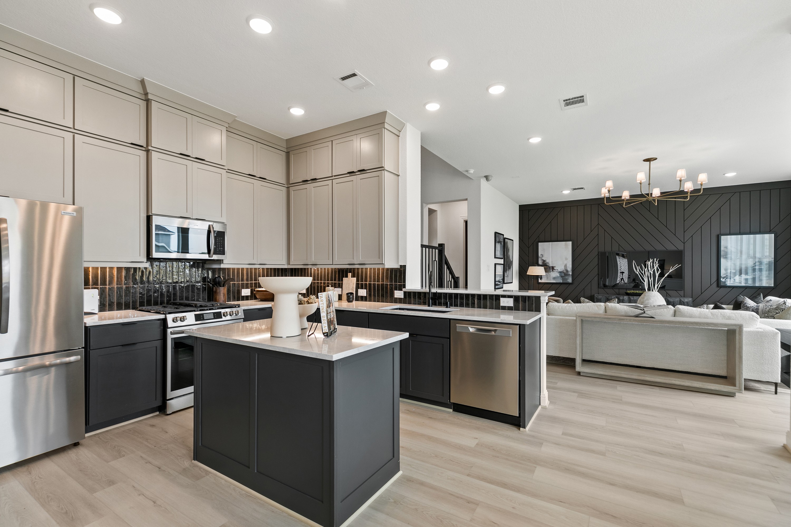 Modern kitchen with island, stainless appliances, open living room, wood accent wall, Park at Eldridge, Texas.