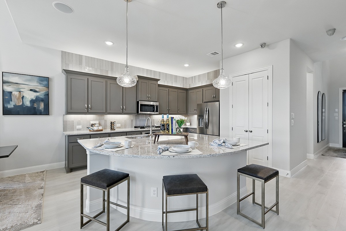Modern kitchen with gray cabinets, granite island, pendant lights in Green Meadows community.