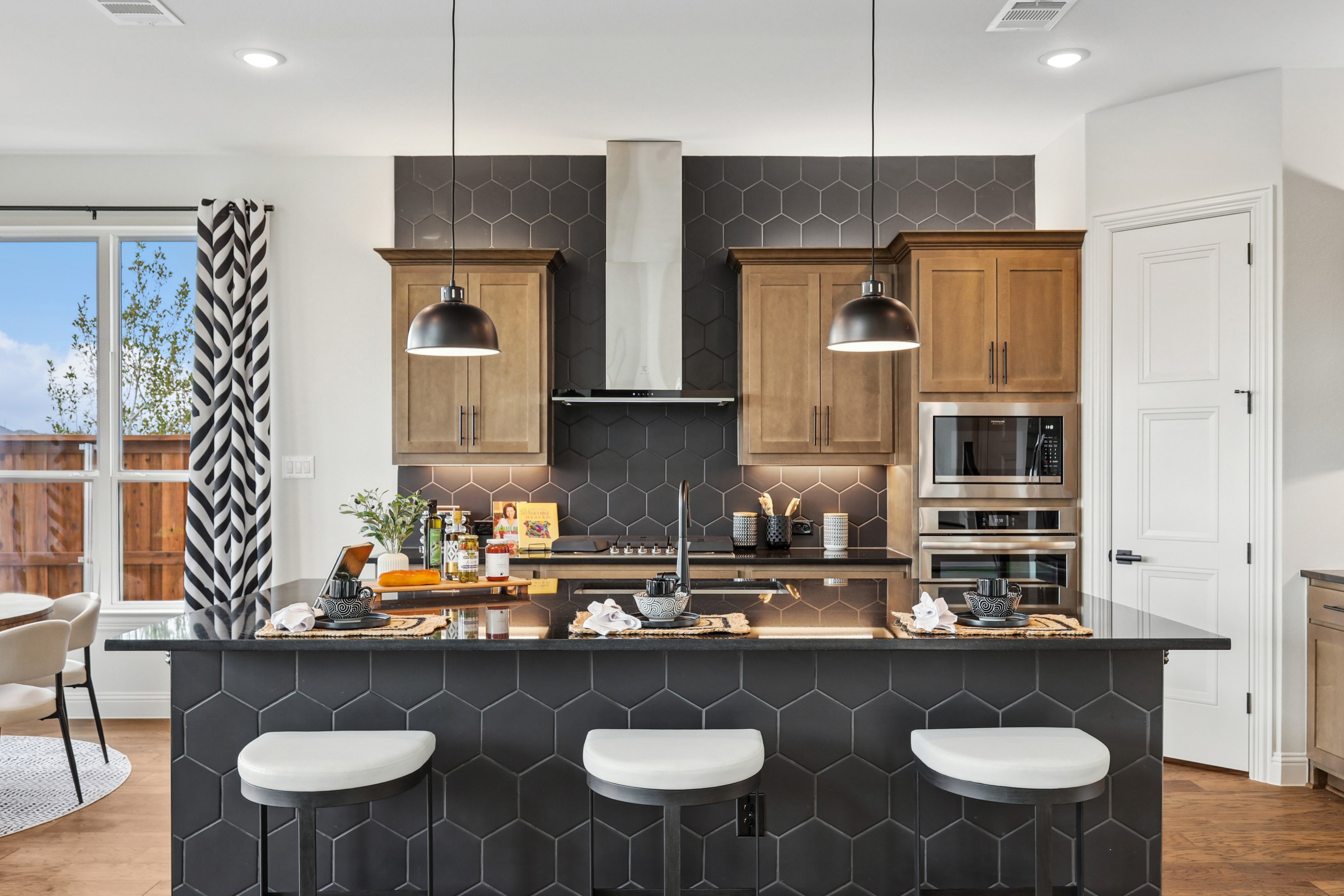 Modern kitchen in Green Meadows; wood cabinets, black hex tiles, stainless appliances, pendant lights.