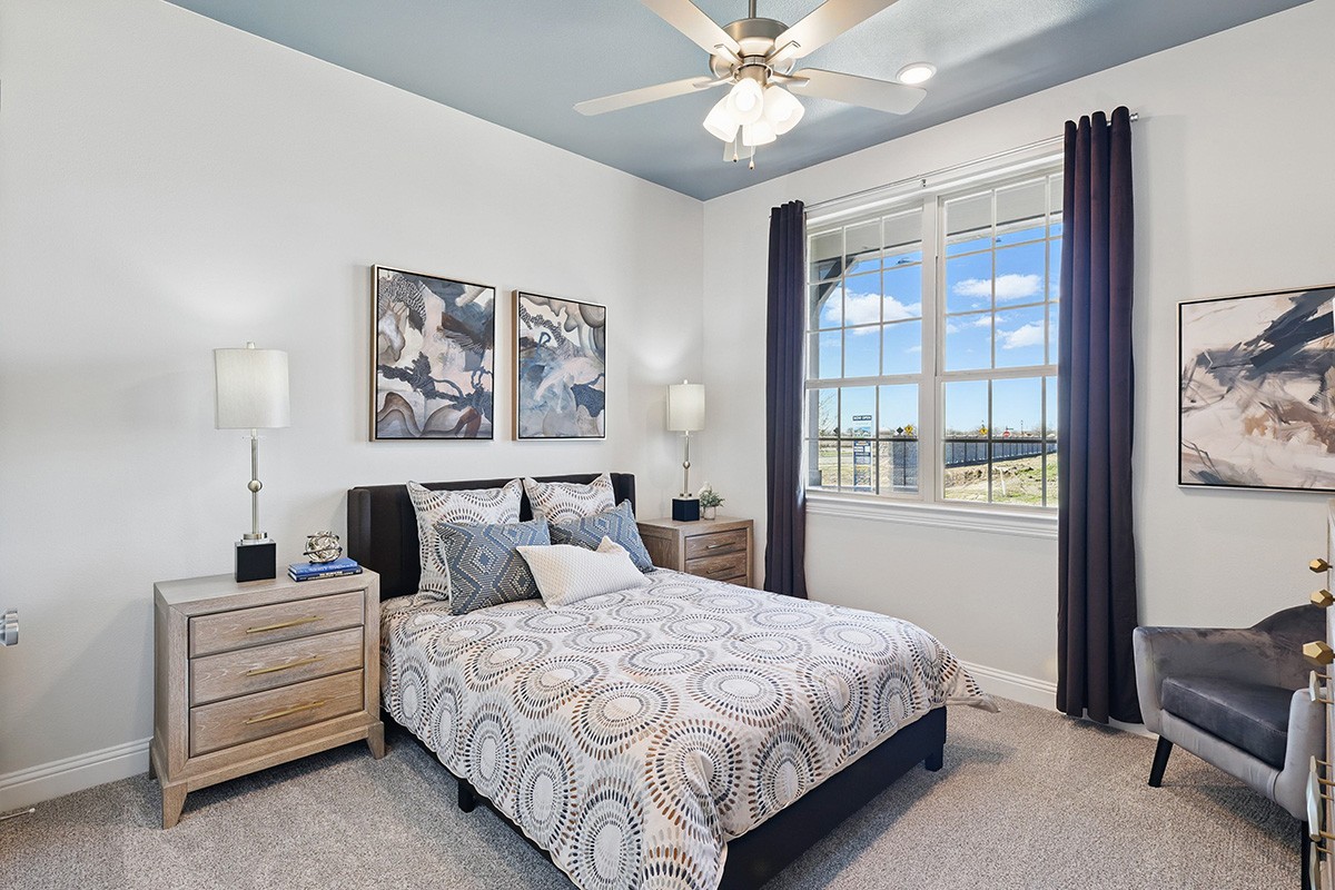 Modern bedroom with abstract art, ceiling fan, and large window in Green Meadows community.