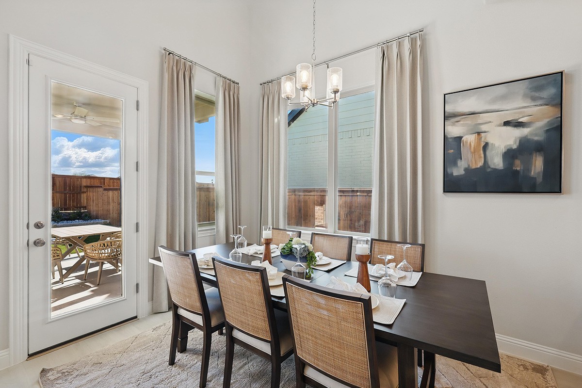 Elegant dining room with chandelier, large windows, and patio view in Green Meadows community.