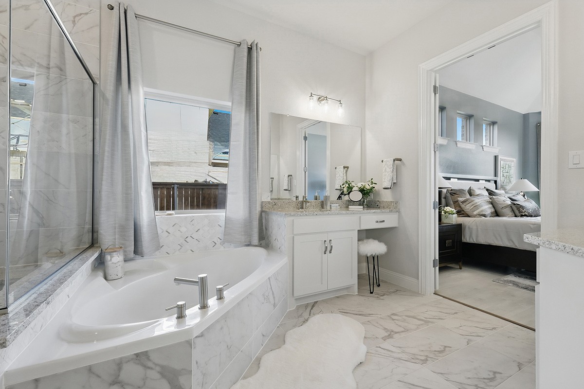 Elegant marble bathroom with soaking tub, vanity, and plush rug. Opens to luxurious bedroom. Green Meadows community.