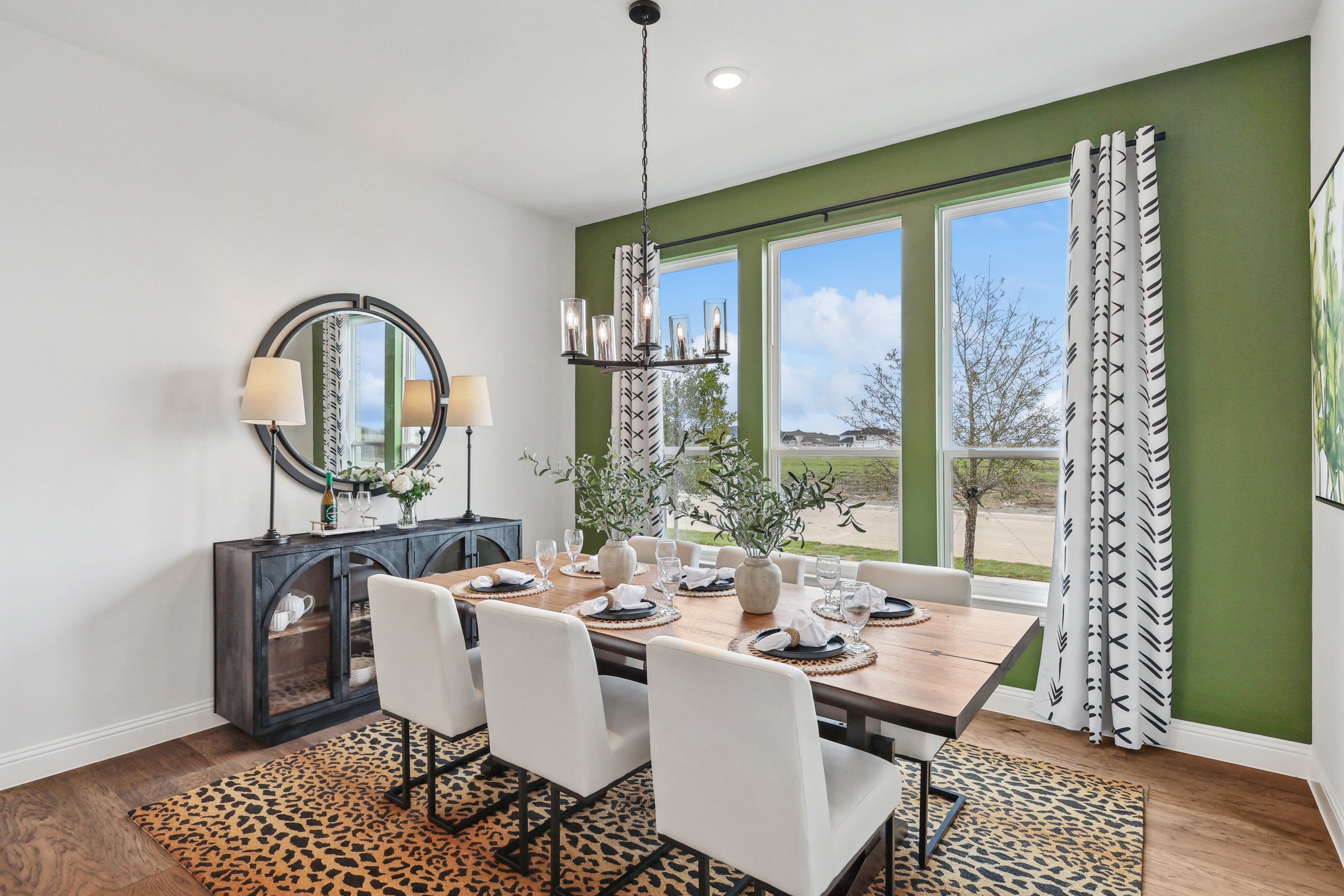 Elegant dining room with wood table, white chairs, green walls in Green Meadows community, featuring large windows.
