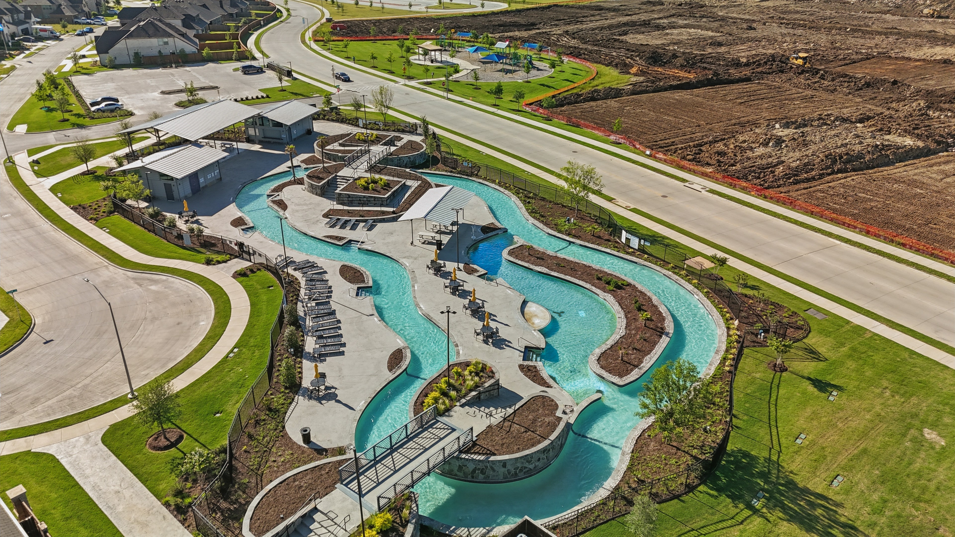 Aerial of luxury lazy river pool, modern architecture in Wildflower Ranch community, landscaped greenery, Texas.