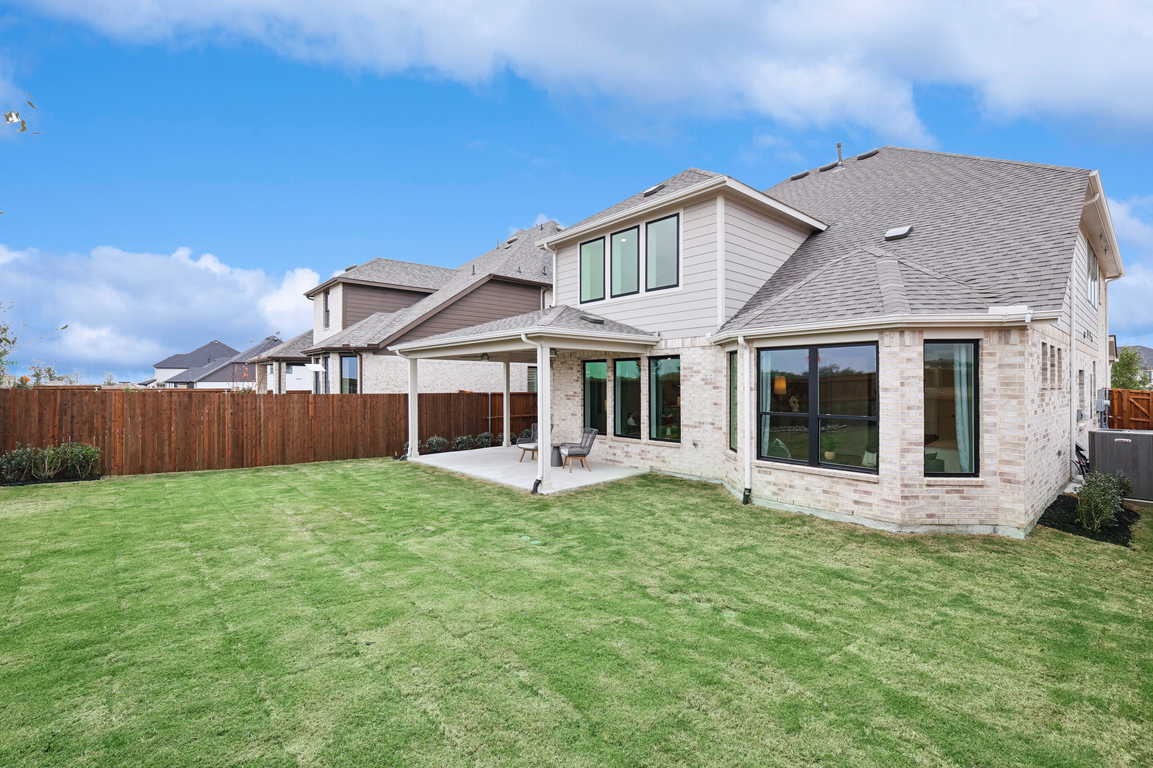 Spacious backyard with covered patio, brick exterior, and manicured lawn in Wildflower Ranch community.