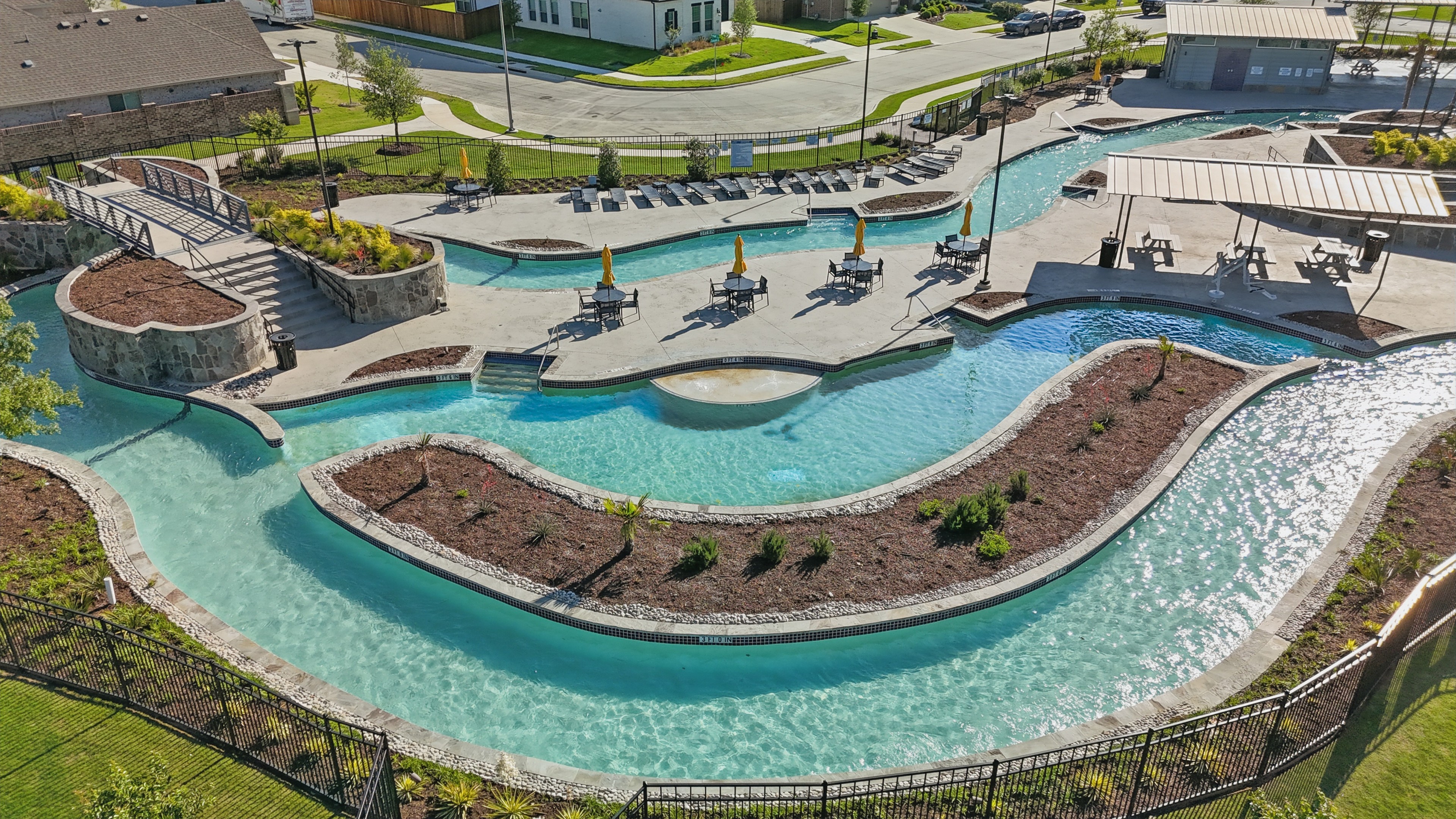 Aerial view of a winding lazy river and pool area with umbrellas at Wildflower Ranch community, Texas.