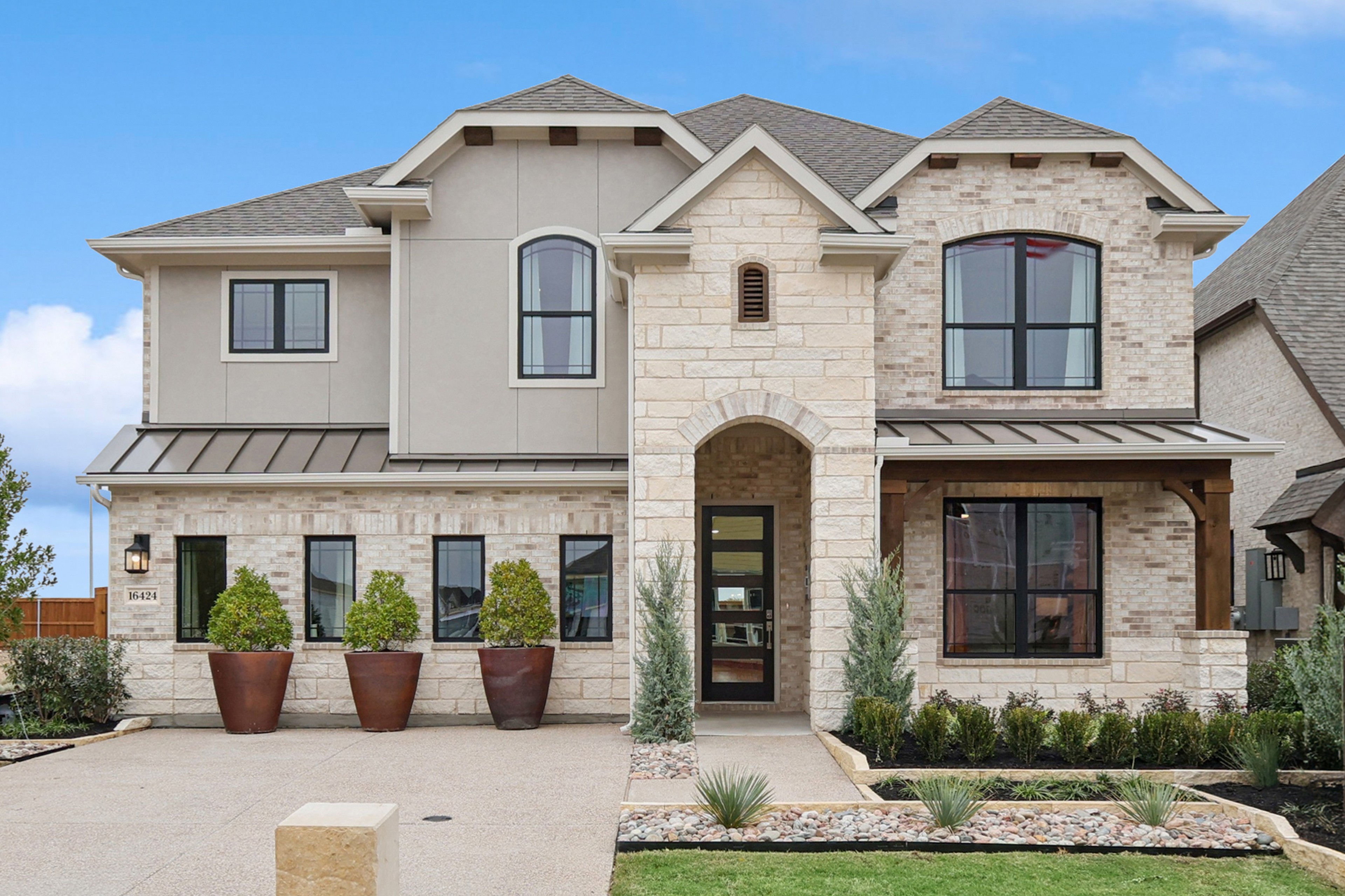 Two-story stone and brick house with arched entry, large windows, modern landscaping, Wildflower Ranch.