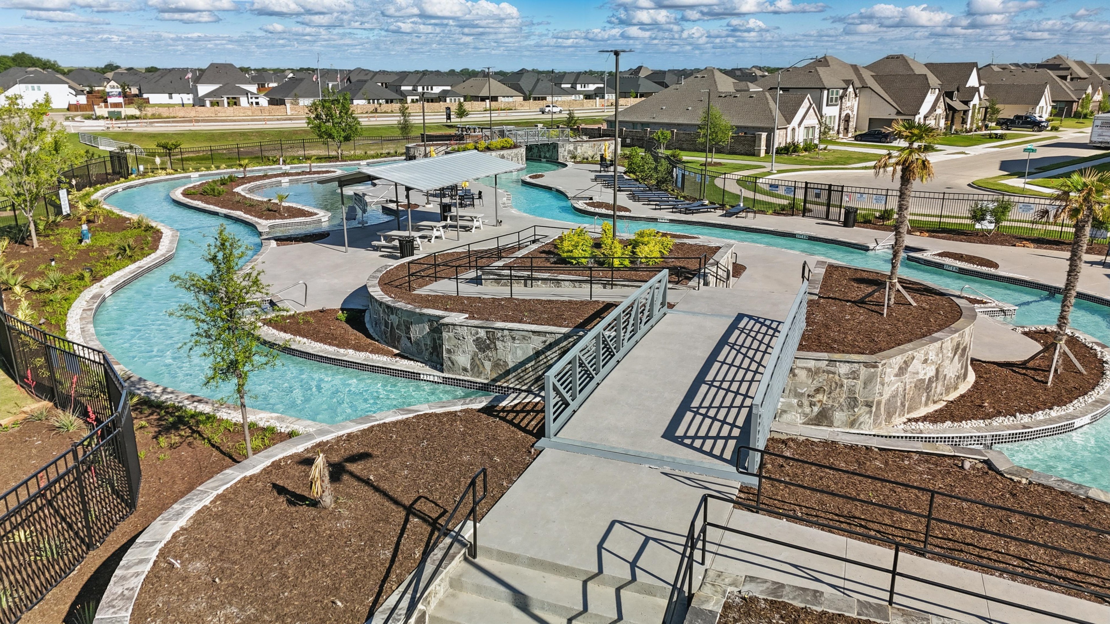 Lazy river at Wildflower Ranch community, Texas. Features stone walls, bridges, lush landscaping, and modern homes.