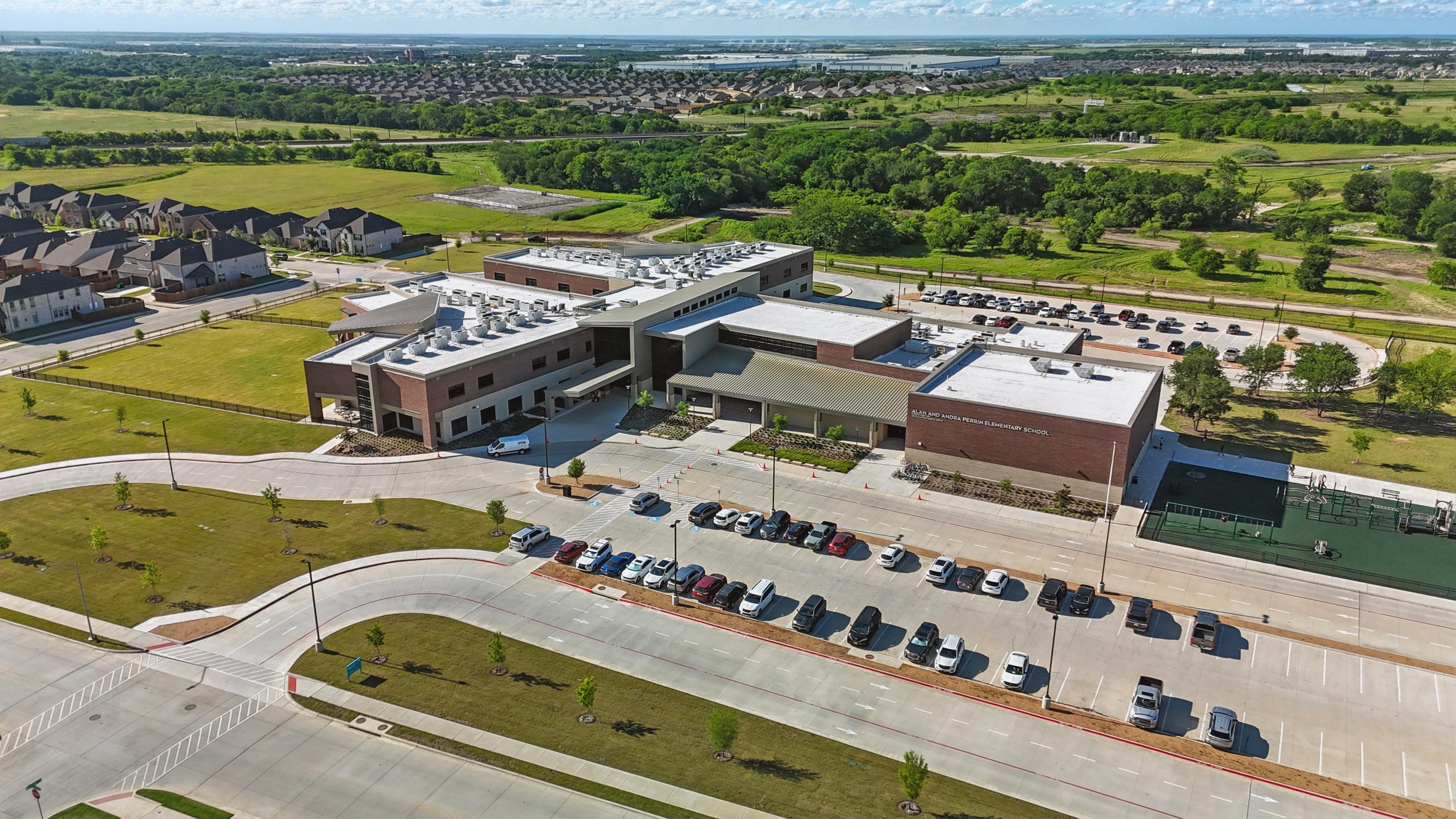 Aerial view of modern school building with parking, surrounded by greenery in Wildflower Ranch community.