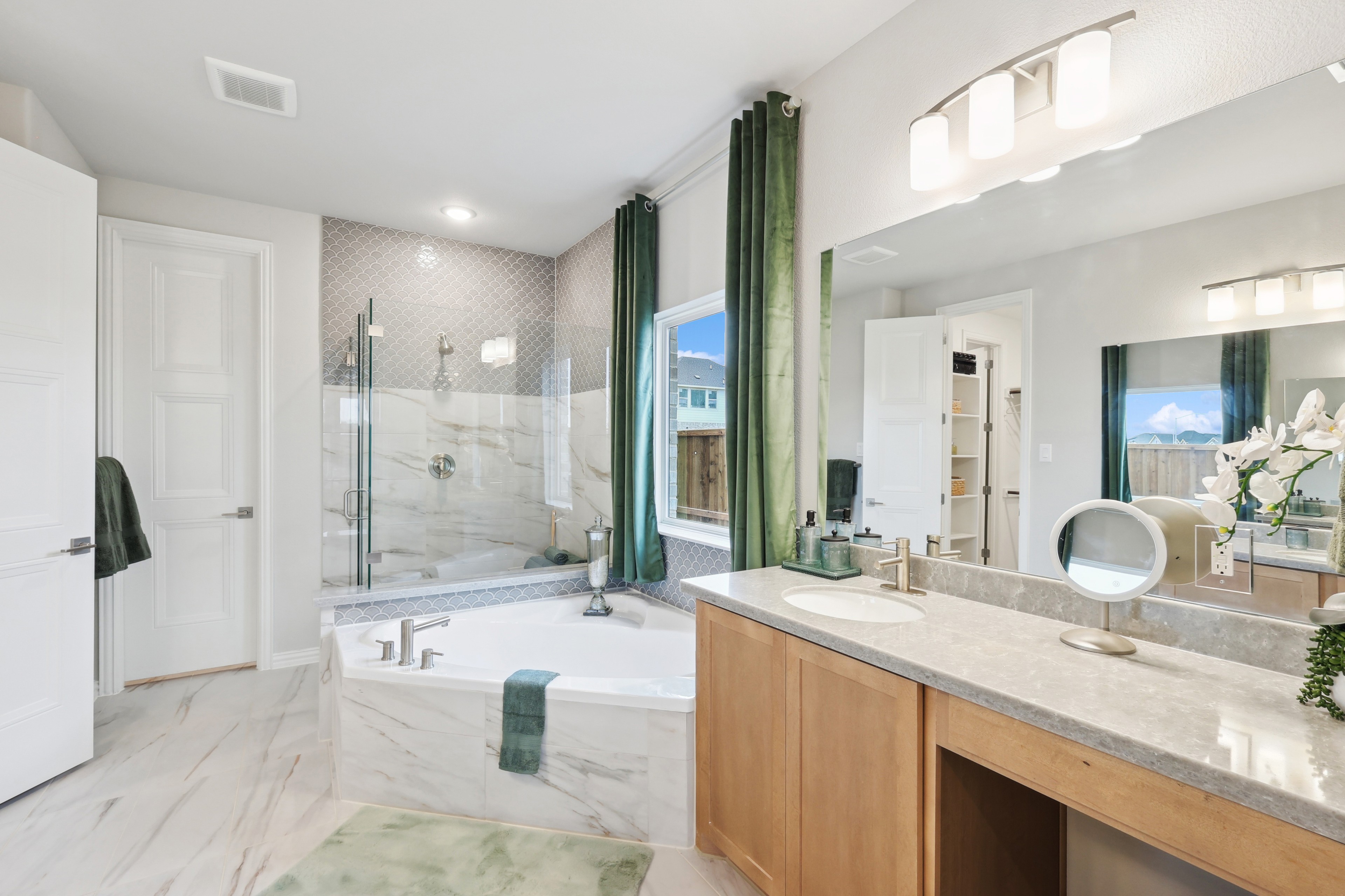 Luxurious bathroom with marble tile, dual vanity, and soaking tub at Wildflower Ranch, featuring large window and green accents.