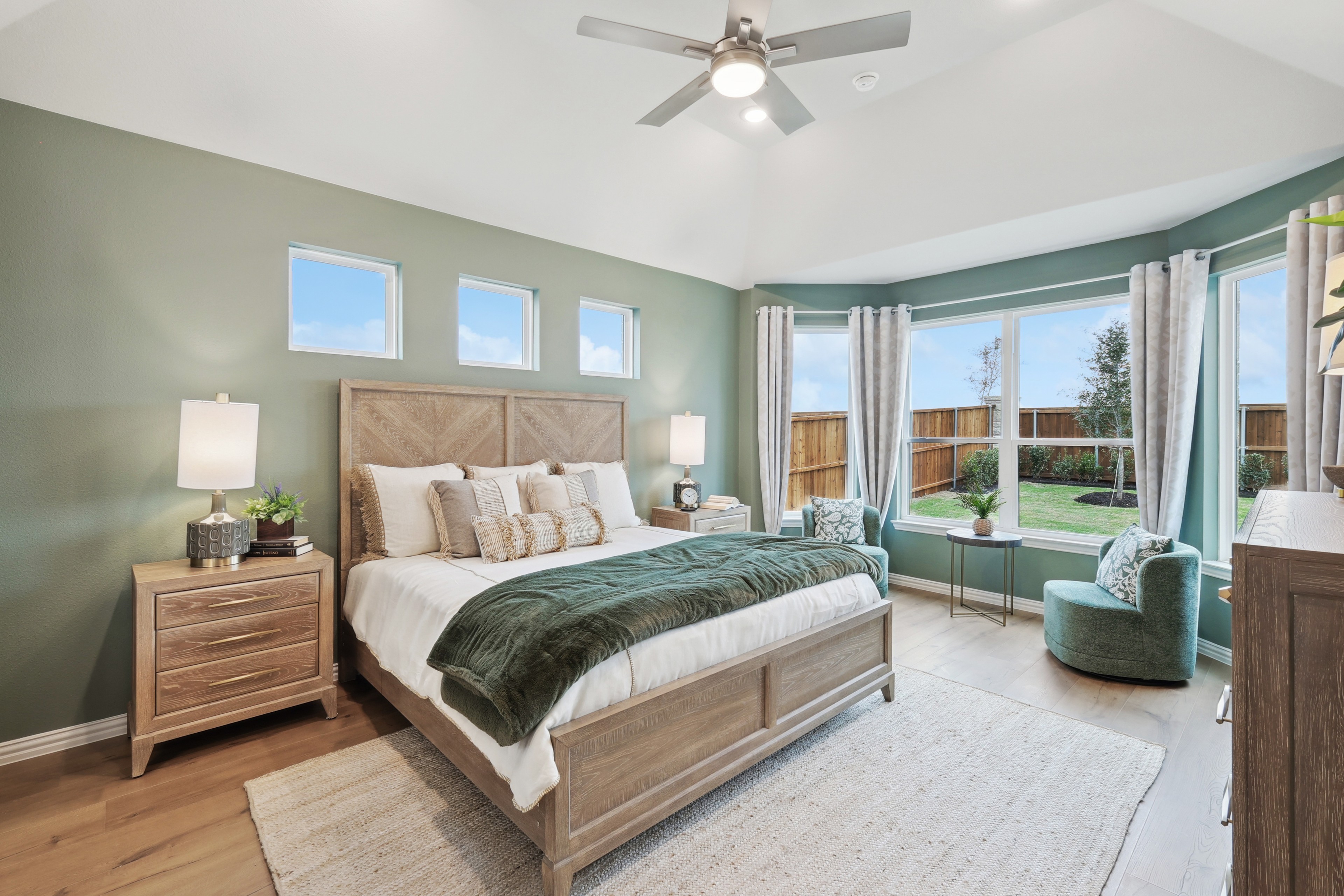 Spacious bedroom with green accent wall, large windows, ceiling fan, wood furniture in Wildflower Ranch.