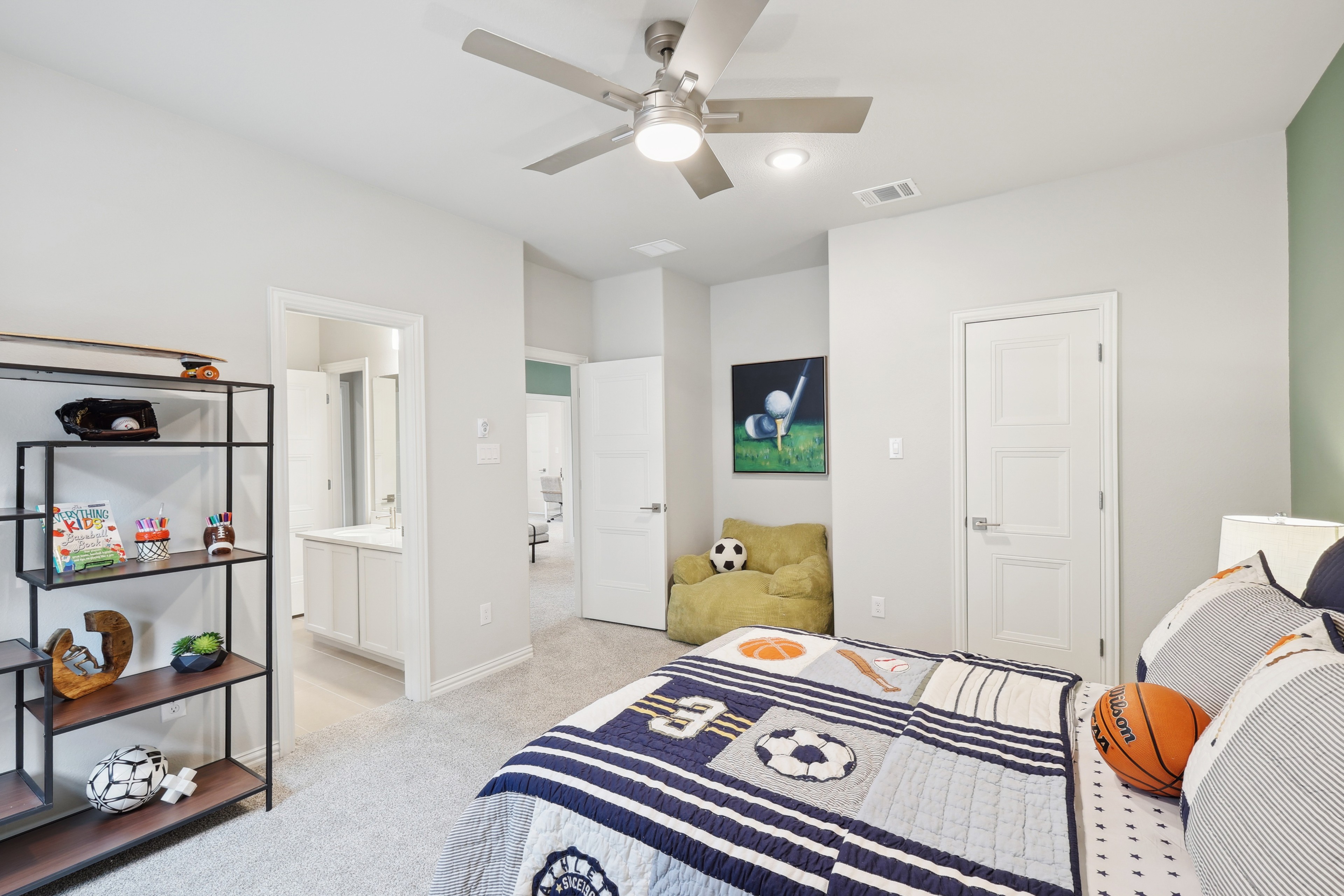 Modern children's bedroom with sports theme, sleek ceiling fan, plush carpet, and ensuite bathroom in Wildflower Ranch.