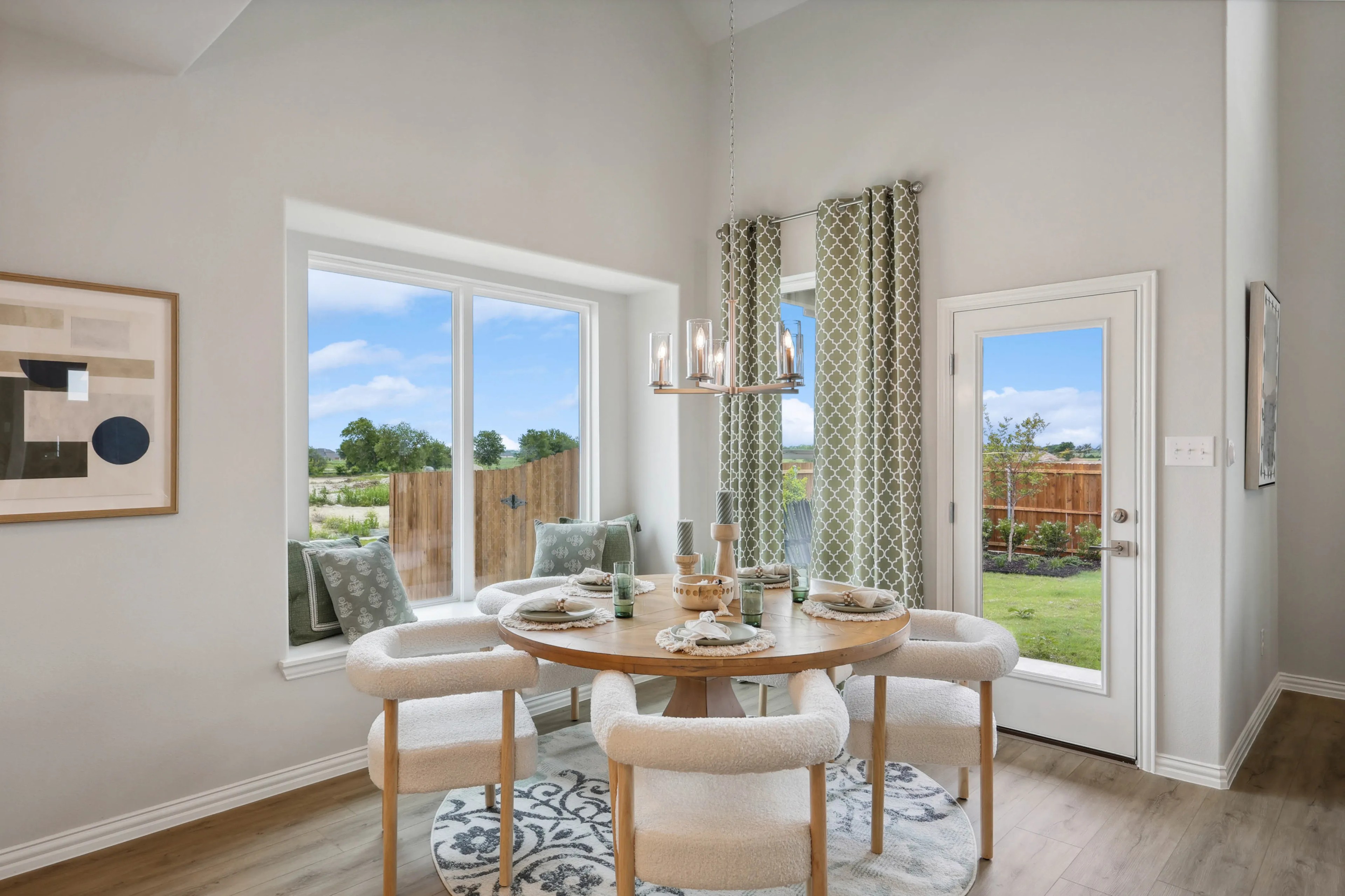 Dining area with round wooden table, plush chairs, large windows, elegant chandelier, and garden view in Hulen Trails.