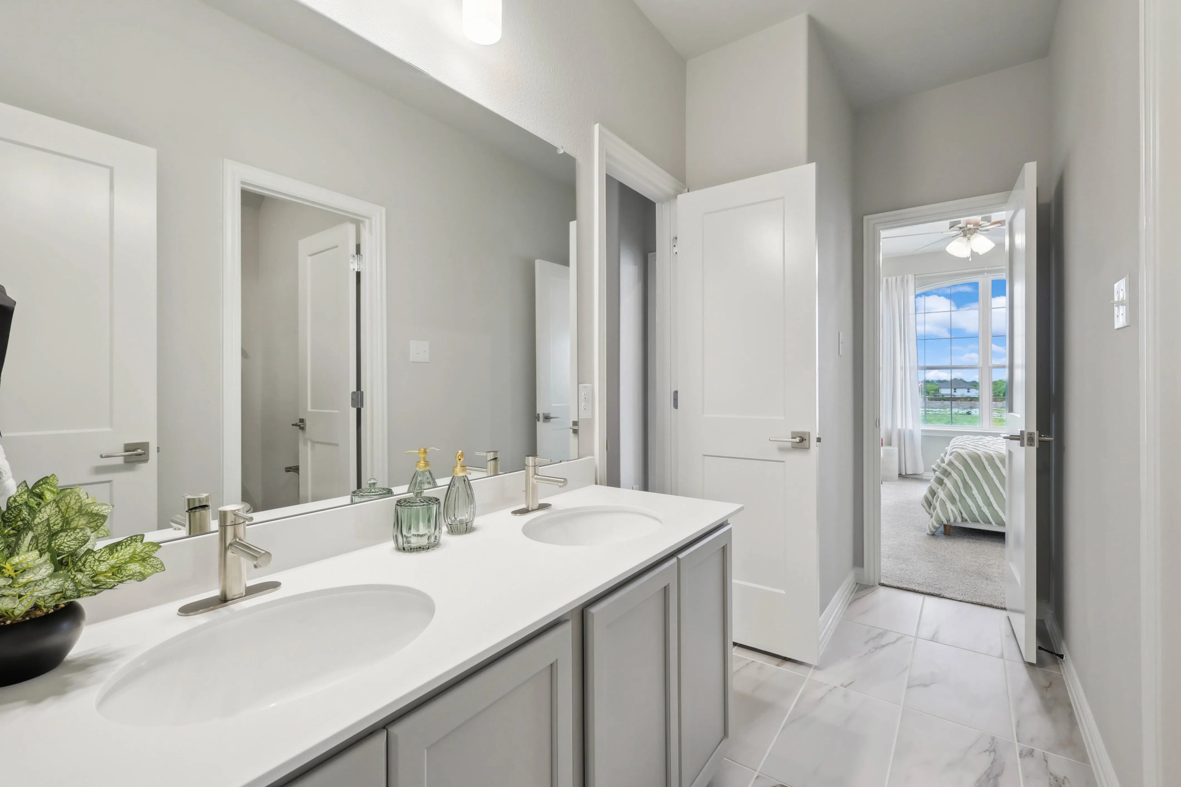 Modern bathroom with double vanity, sleek fixtures, adjacent bedroom view, Hulen Trails home.