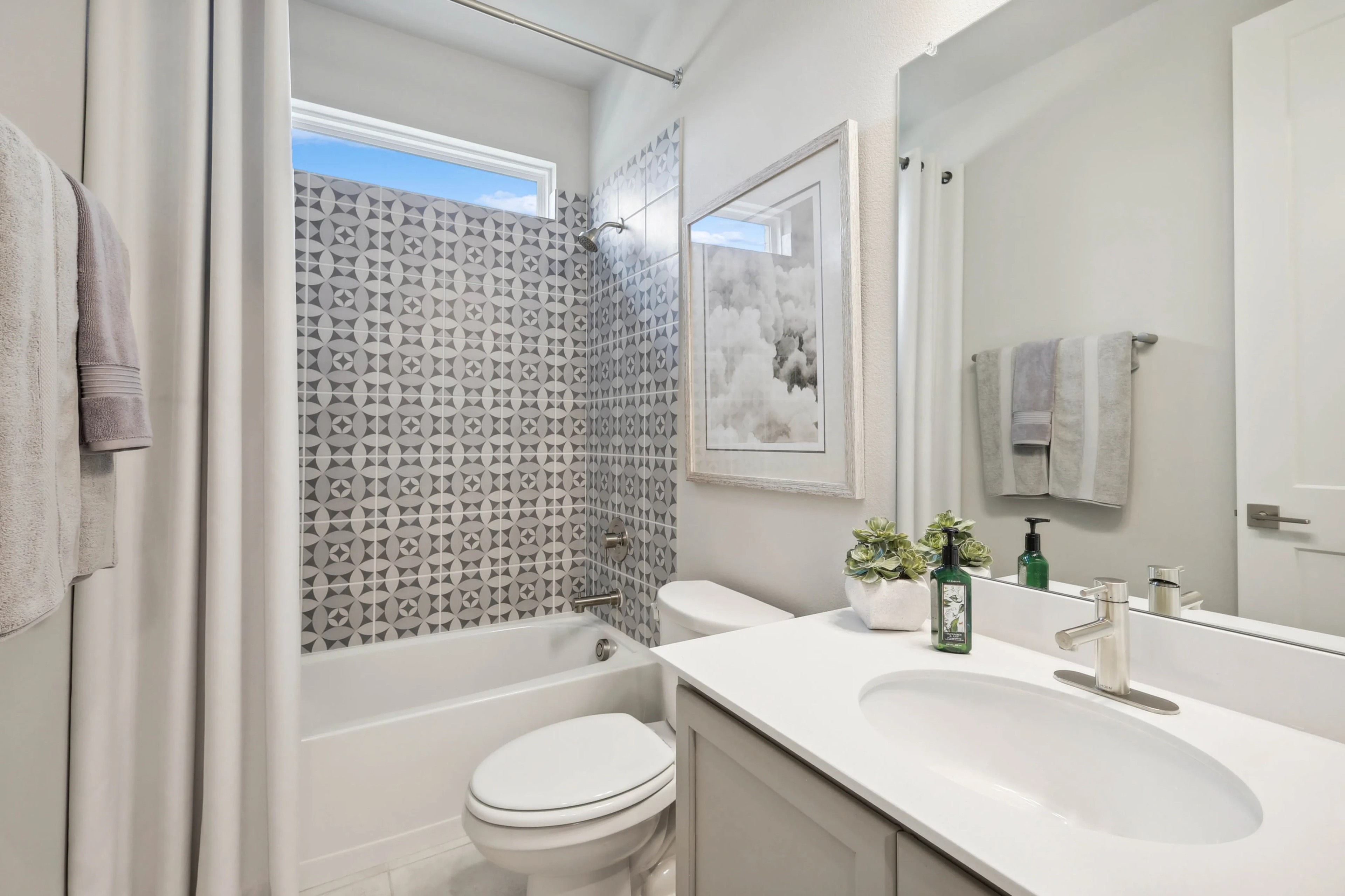 Modern bathroom with geometric tile, framed artwork, and white fixtures in Hulen Trails.
