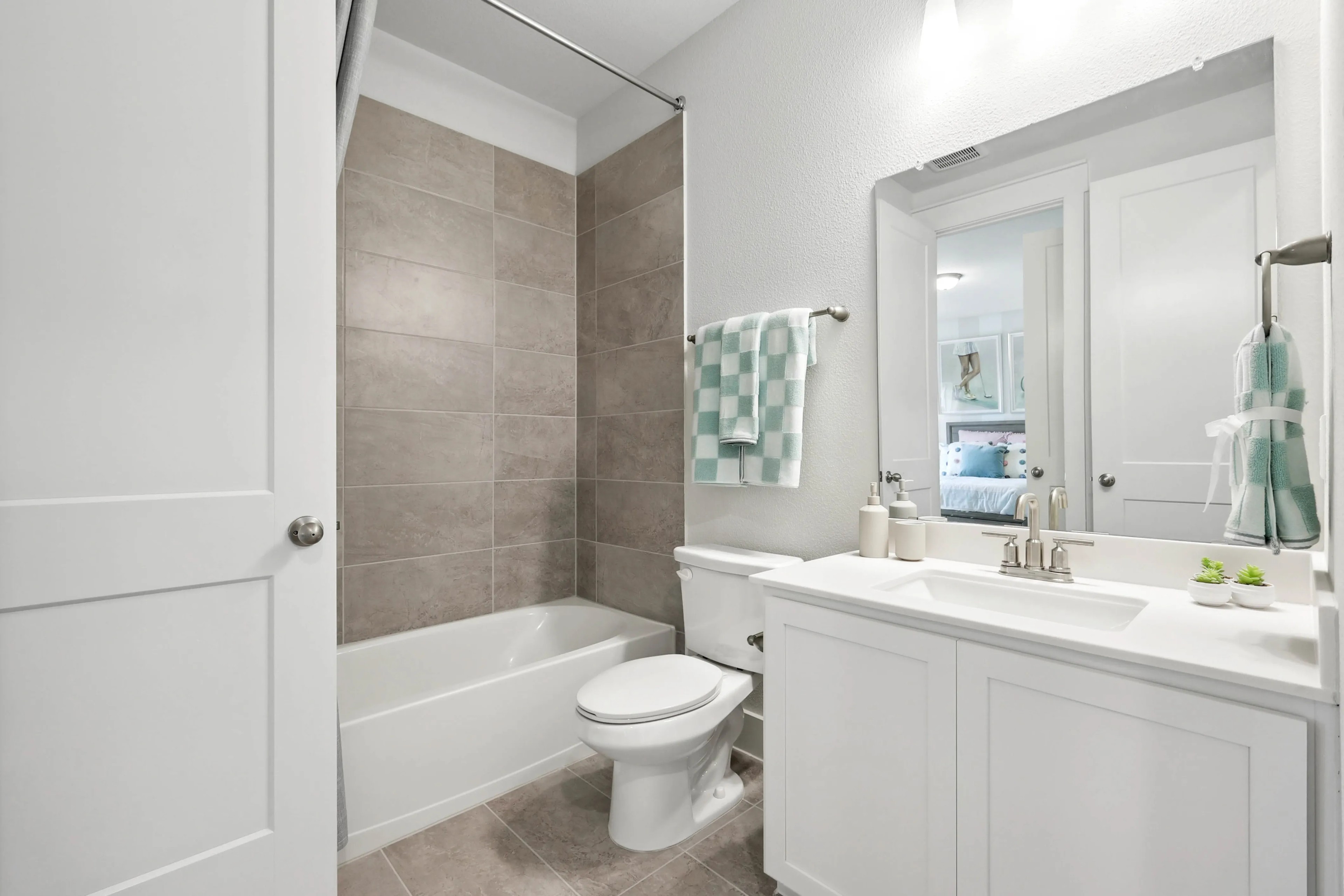 Modern bathroom with white vanity, tile shower, and large mirror in Collin Creek community.