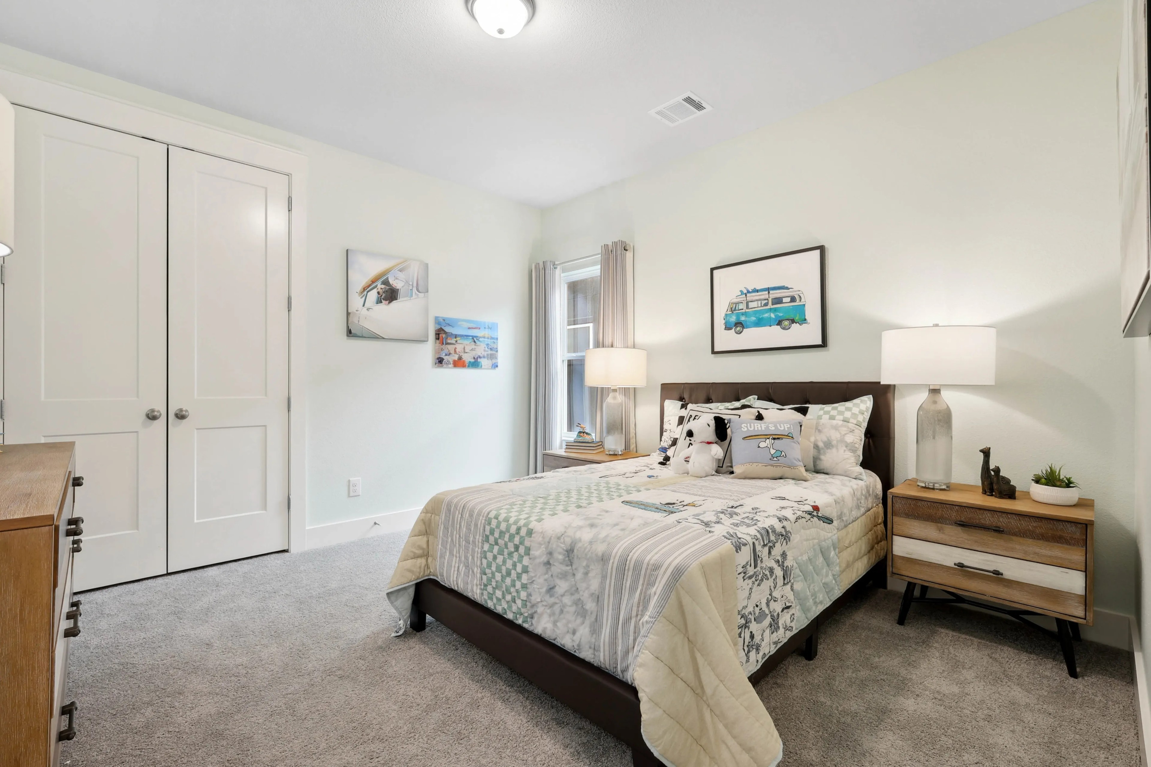 Modern bedroom with cozy decor, featuring a bed with patterned bedding, nightstand, artwork, and soft carpet in Collin Creek.