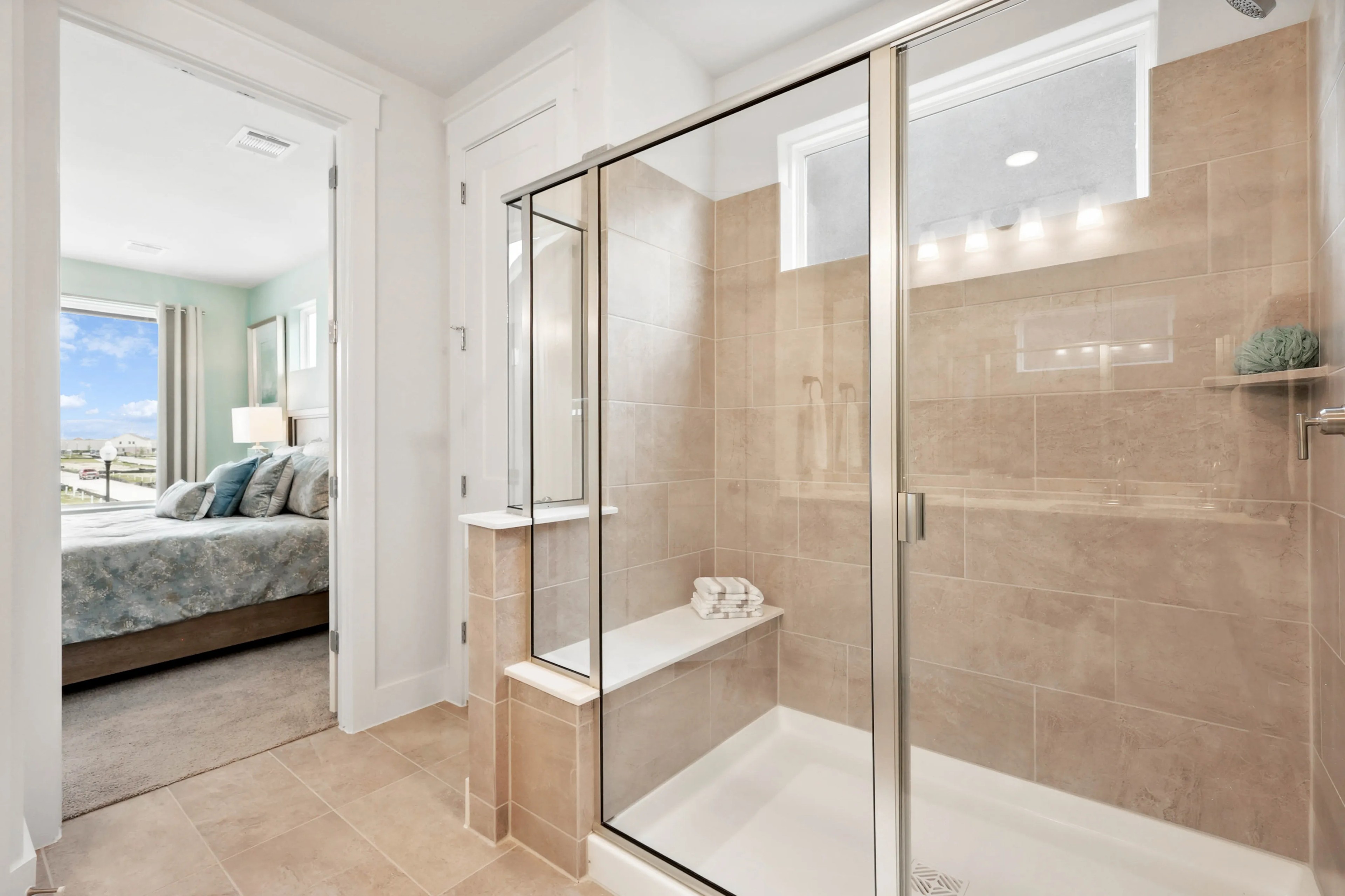 Luxurious Collin Creek bathroom with glass-enclosed shower, beige tiles, adjacent elegant bedroom.