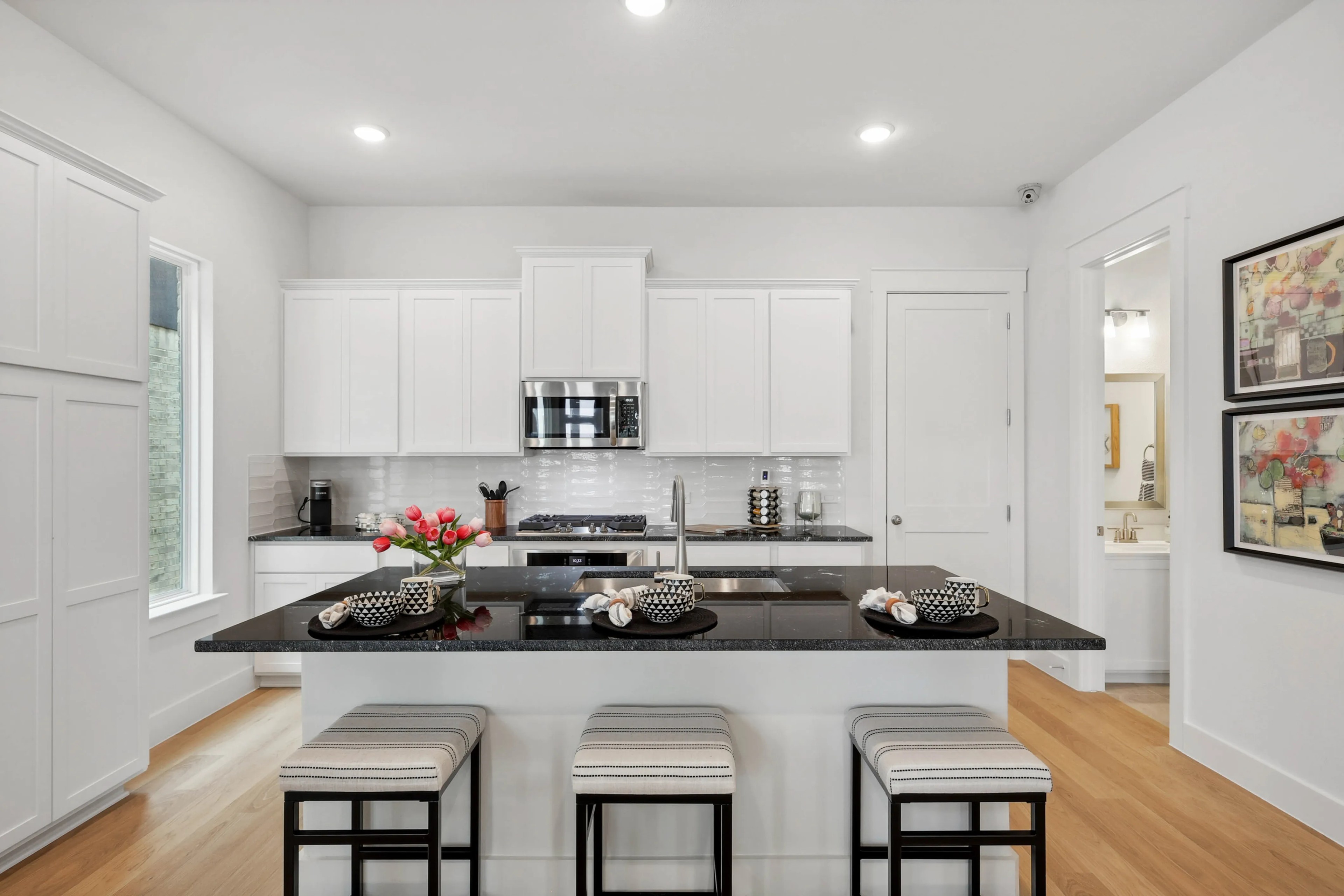 Modern kitchen in Collin Creek with white cabinets, granite island, hardwood floors, and bar seating.