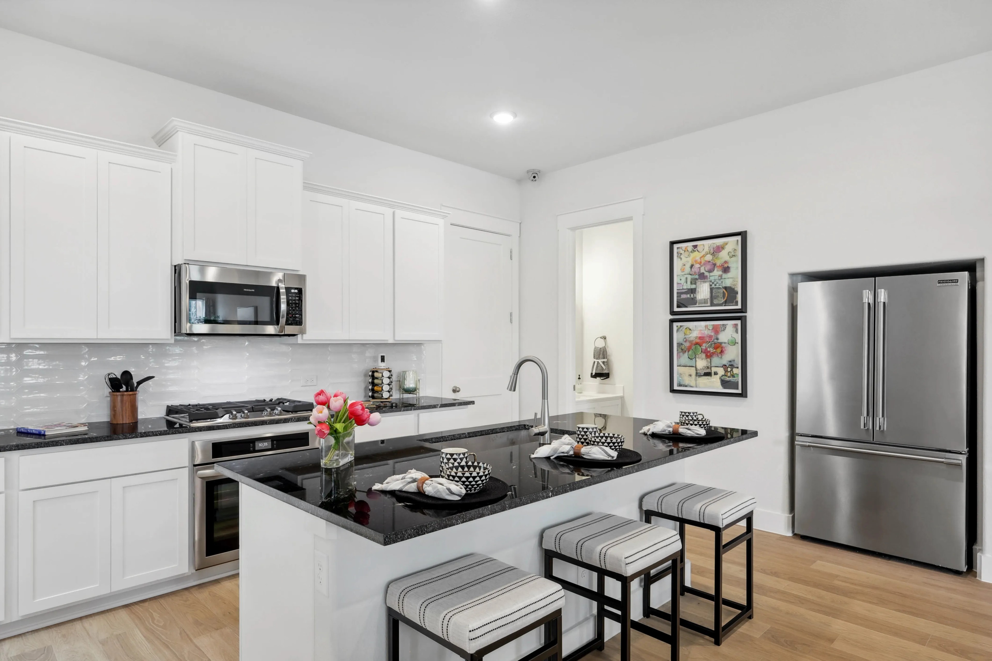 Modern kitchen with sleek black granite island, stainless appliances, white cabinets in Collin Creek community.