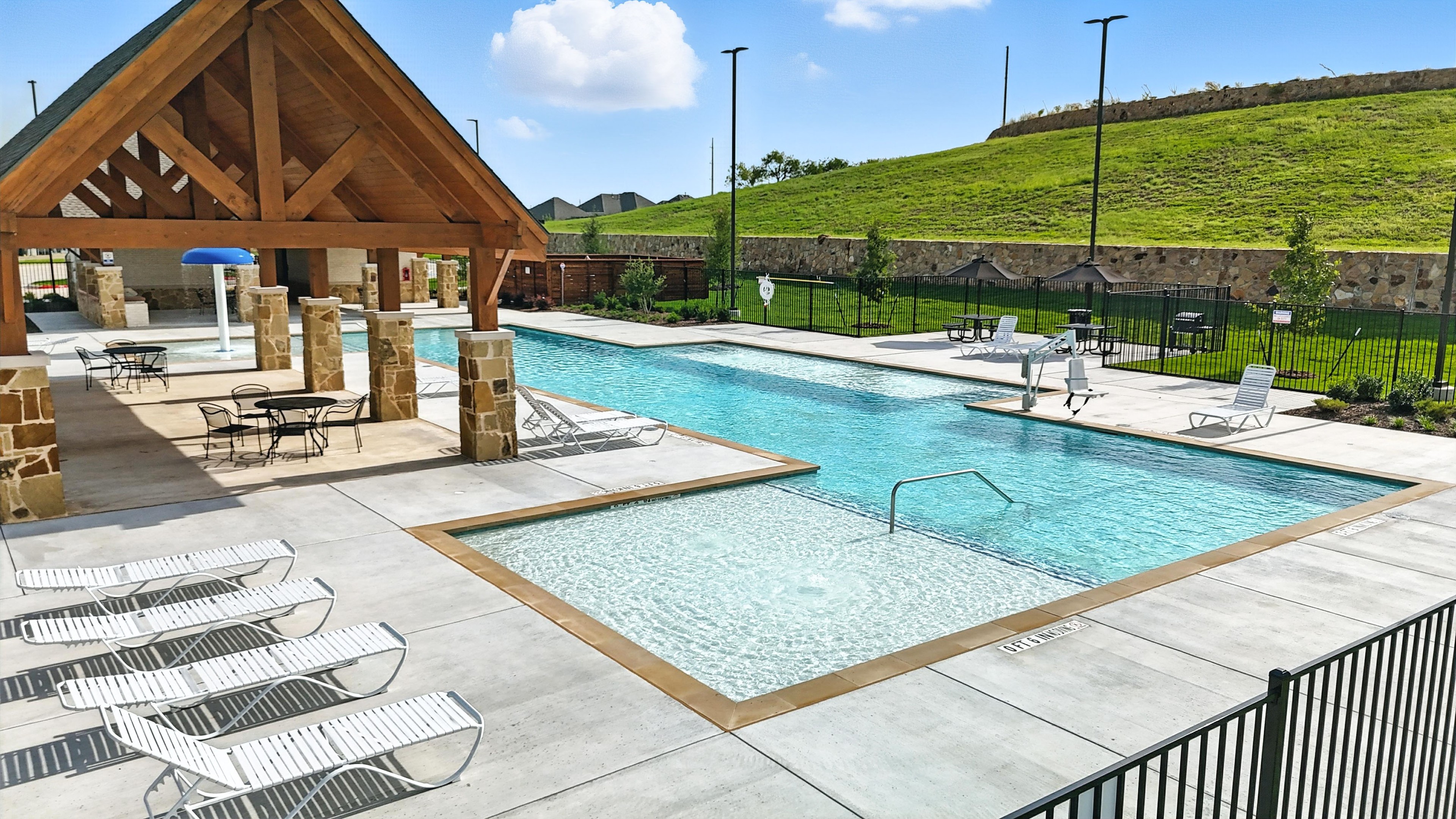 Modern pool with wooden pavilion and stone pillars at Westside Preserve community, surrounded by greenery. Relaxing space.