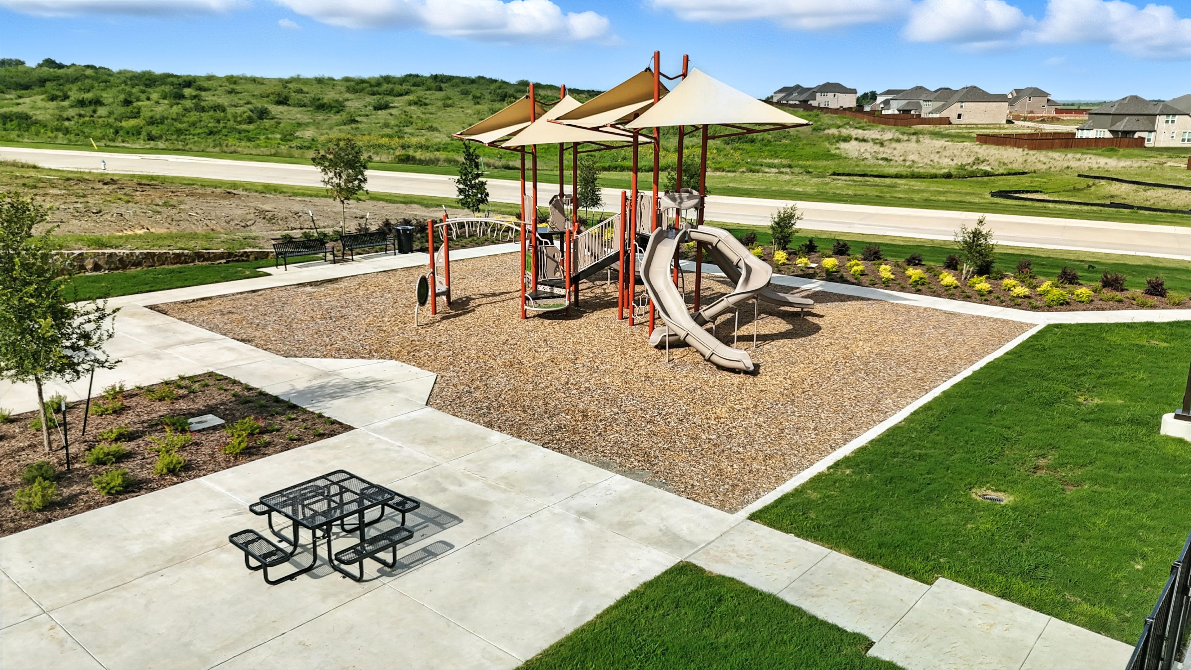 Playground with slides, shade structures, in Westside Preserve community; open green landscape, nearby road.