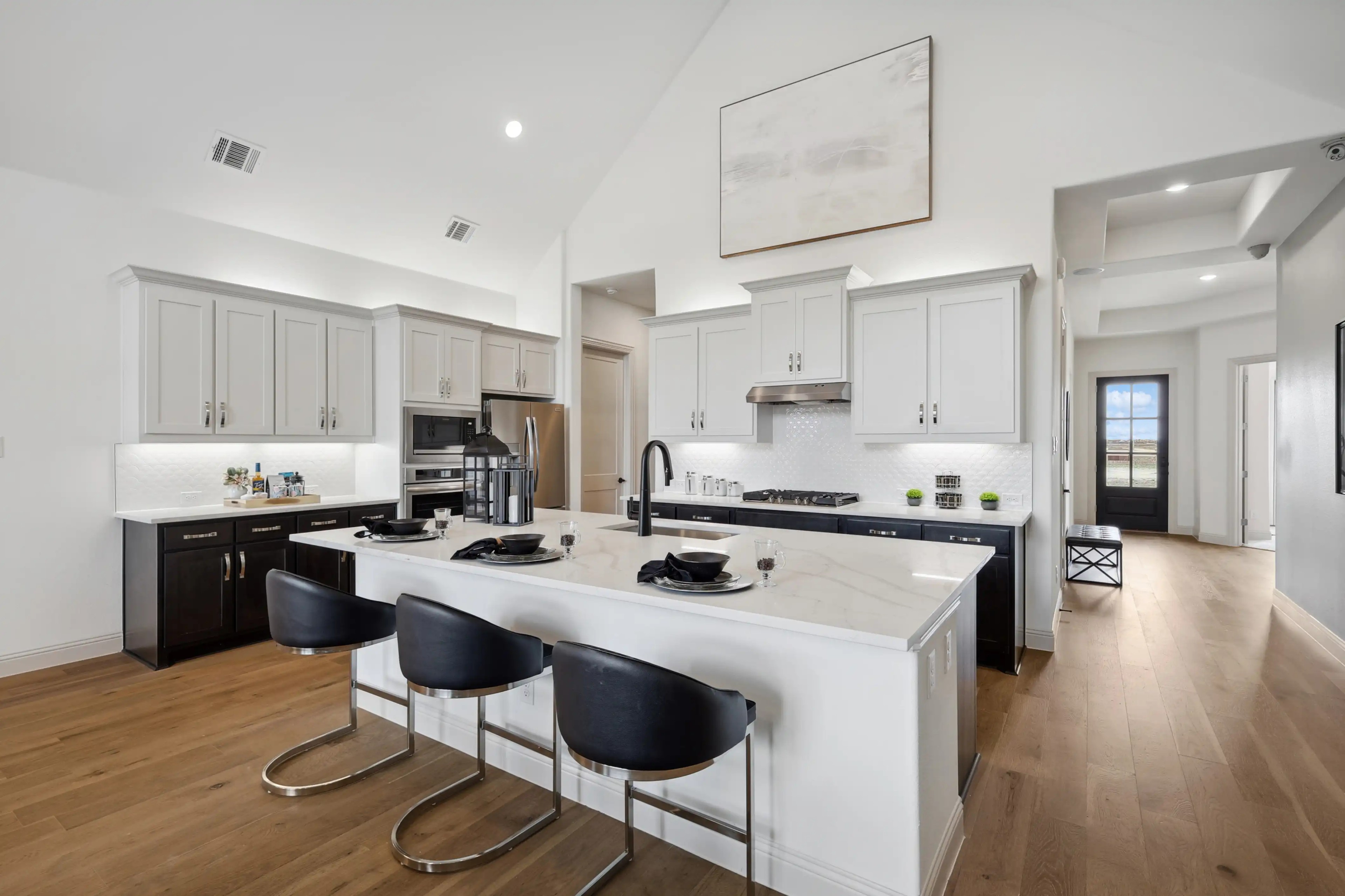 Luxury kitchen with white cabinets, marble island, hardwood floors, and stainless appliances in Westside Preserve home.