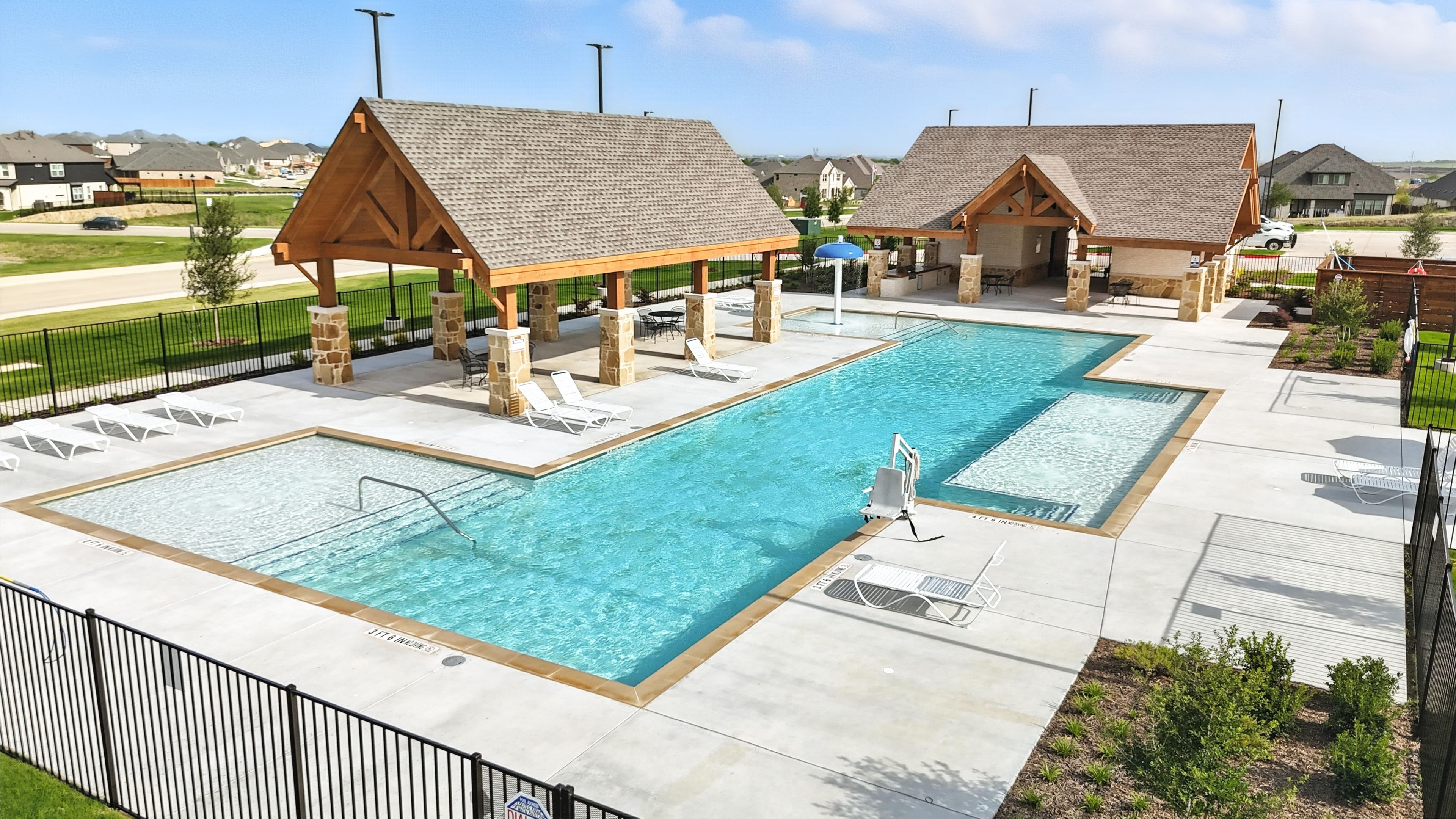 Luxurious pool with stone cabanas, wood detailing, fenced area in Westside Preserve community. Suburban backdrop.