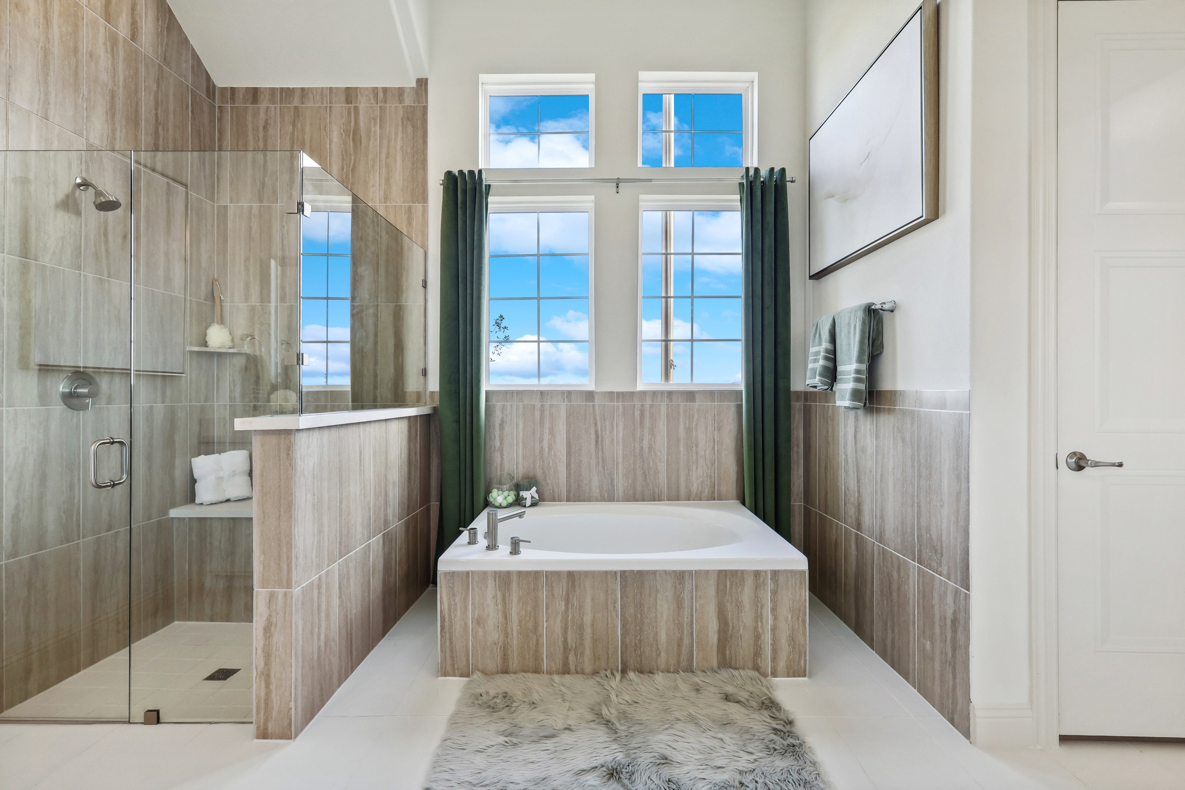 Luxurious bathroom in Solterra, Texas with glass shower, jetted tub, tiled walls, and large windows with sky view.