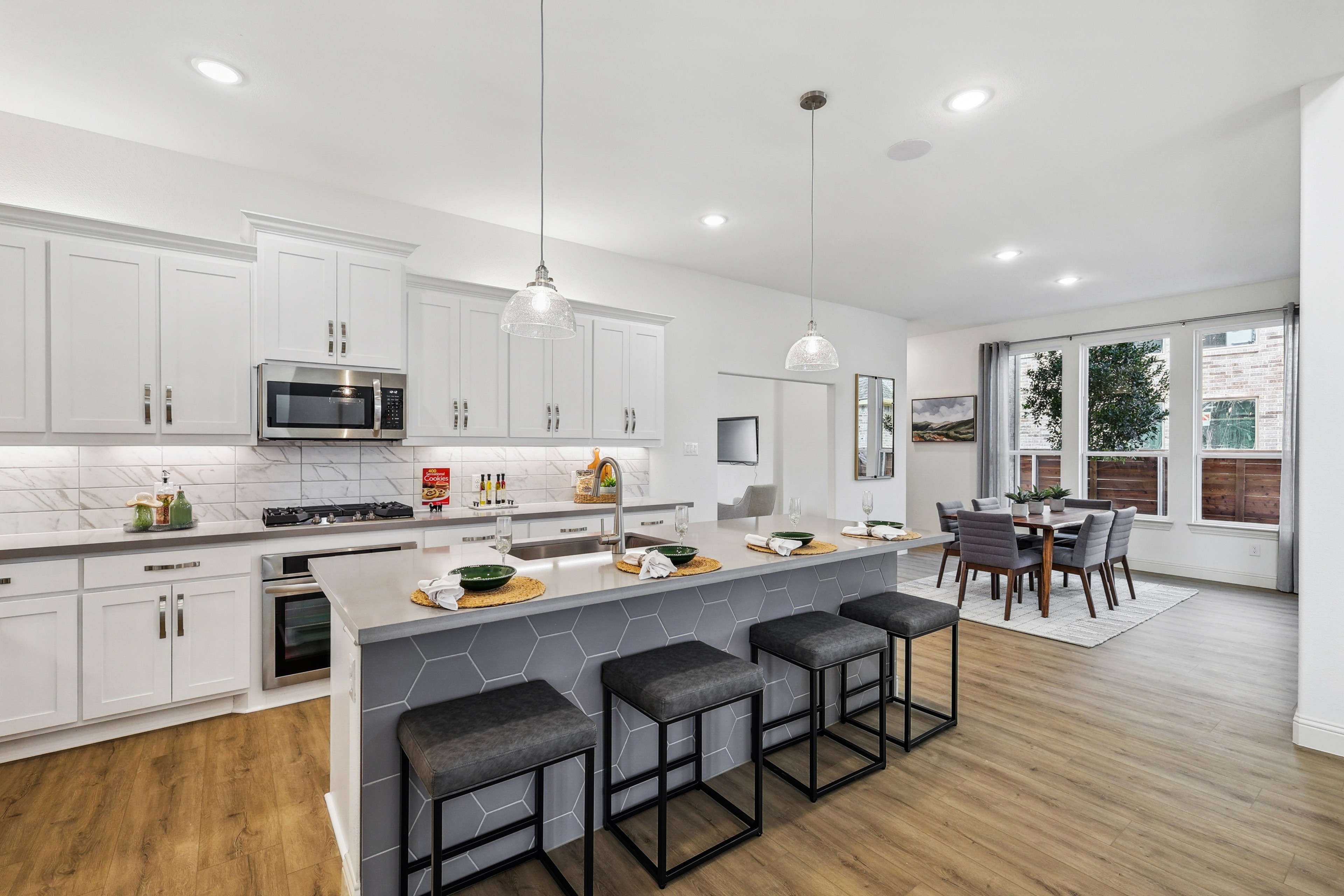 Modern kitchen with hexagon tile island, white cabinets, pendant lights, and open dining area in Solterra Texas home.