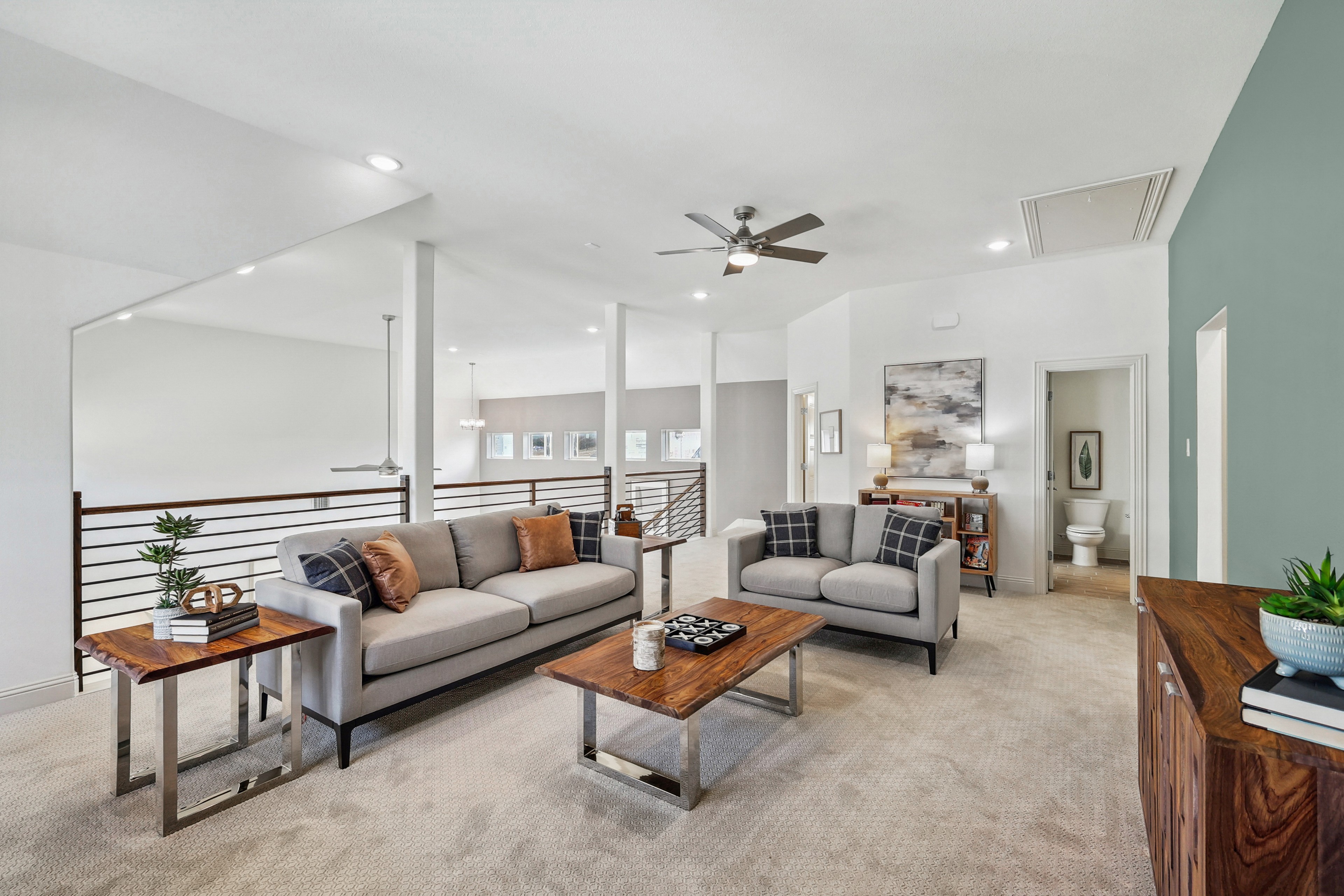 Modern Texas lounge with plush sofas, wooden tables, ceiling fan, neutral tones, and railing. Located in Solterra community.