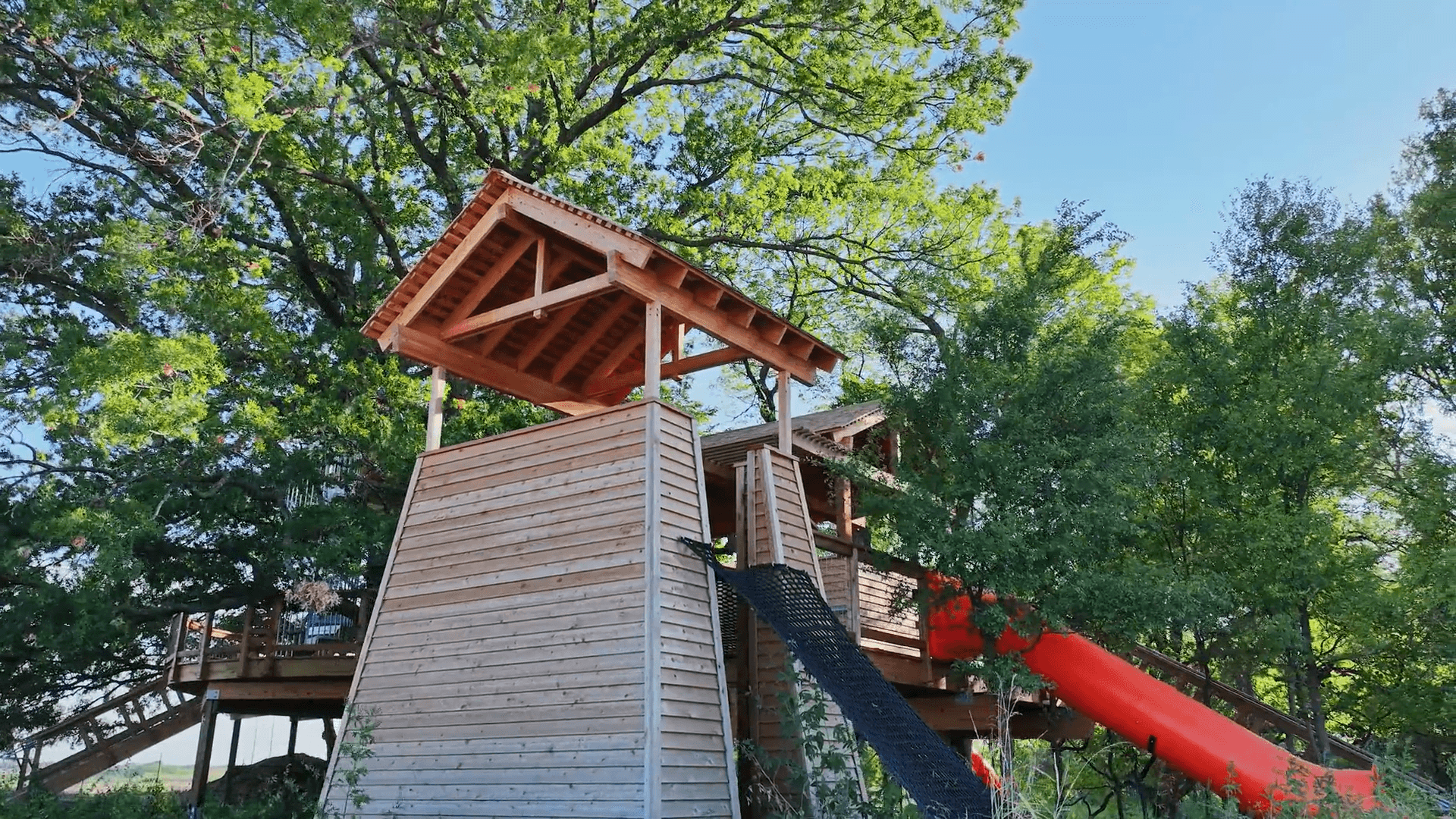 Wooden treehouse with slide, rope bridge in lush Texas trees at Solterra community.