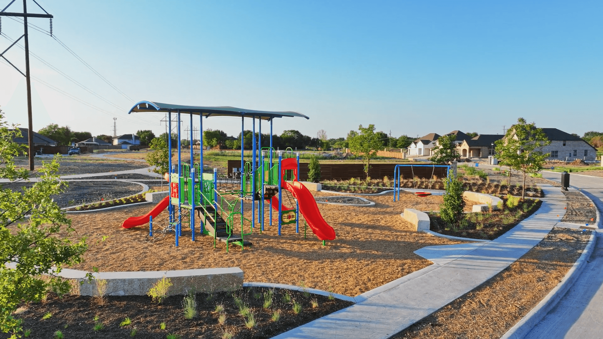 Playground with slides and swings, surrounded by pathways and young trees in Solterra, Texas community park.