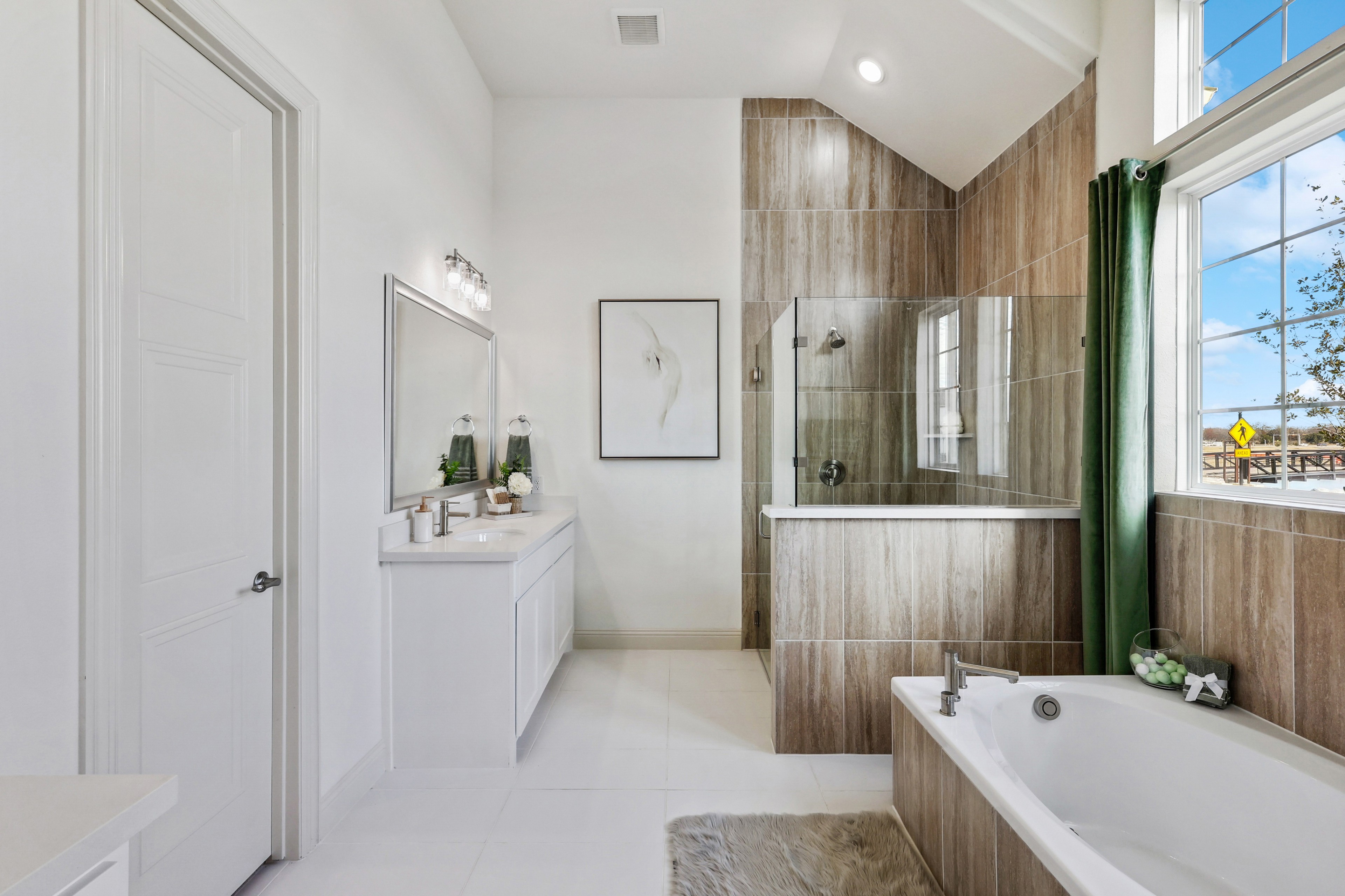 Luxurious bathroom with glass shower, tub, large mirror, and contemporary decor in Solterra, Texas. Bright natural light.