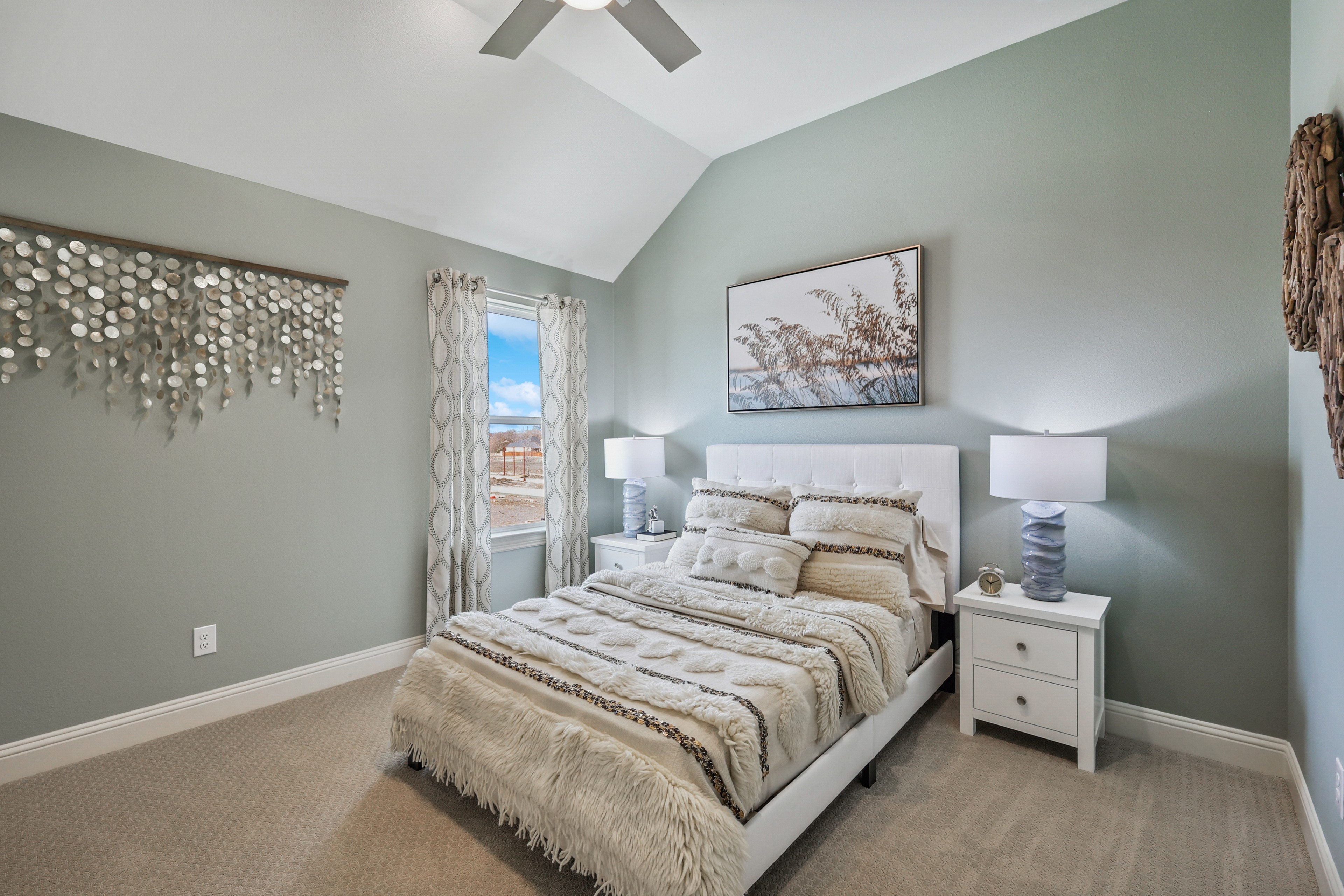 Stylish bedroom in Solterra Texas with vaulted ceiling, modern decor, and soft tones. Large window offers natural light.