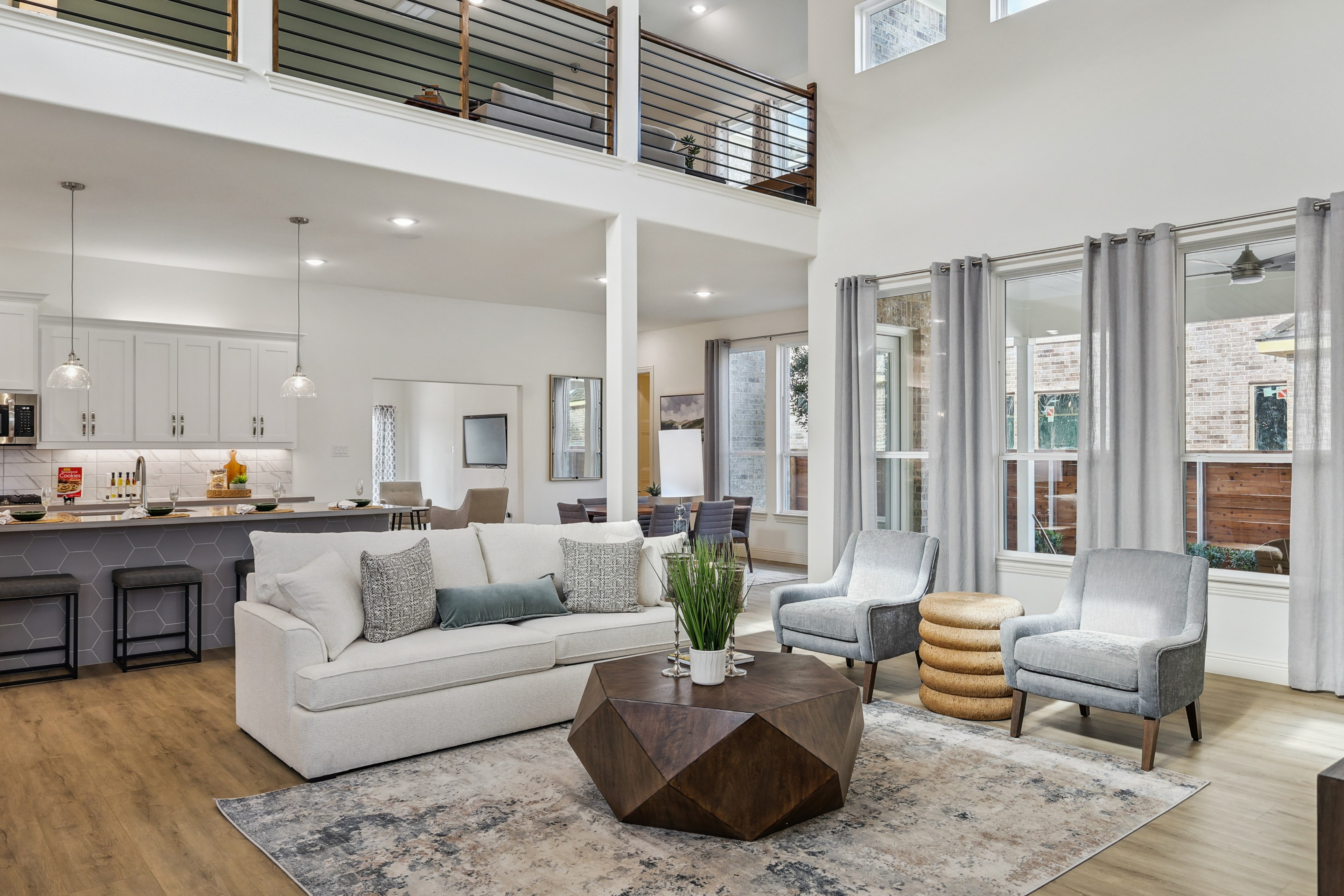 Open-plan Texas living room with wood floors, modern furnishings, large windows, and sleek railing. Solterra community.
