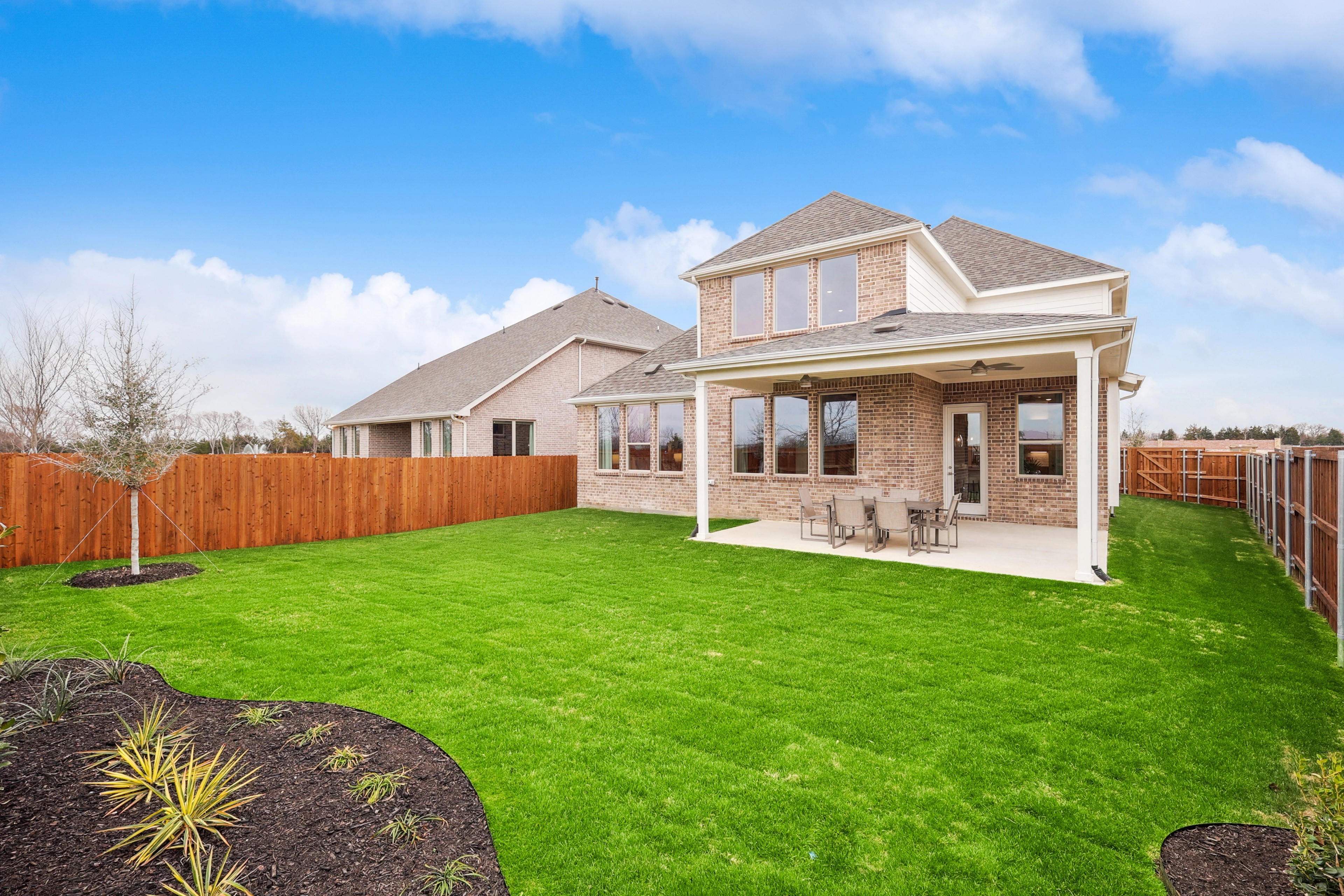 Brick house with large backyard, patio, and wooden fence in The Oaks community. Clean design, spacious exterior.
