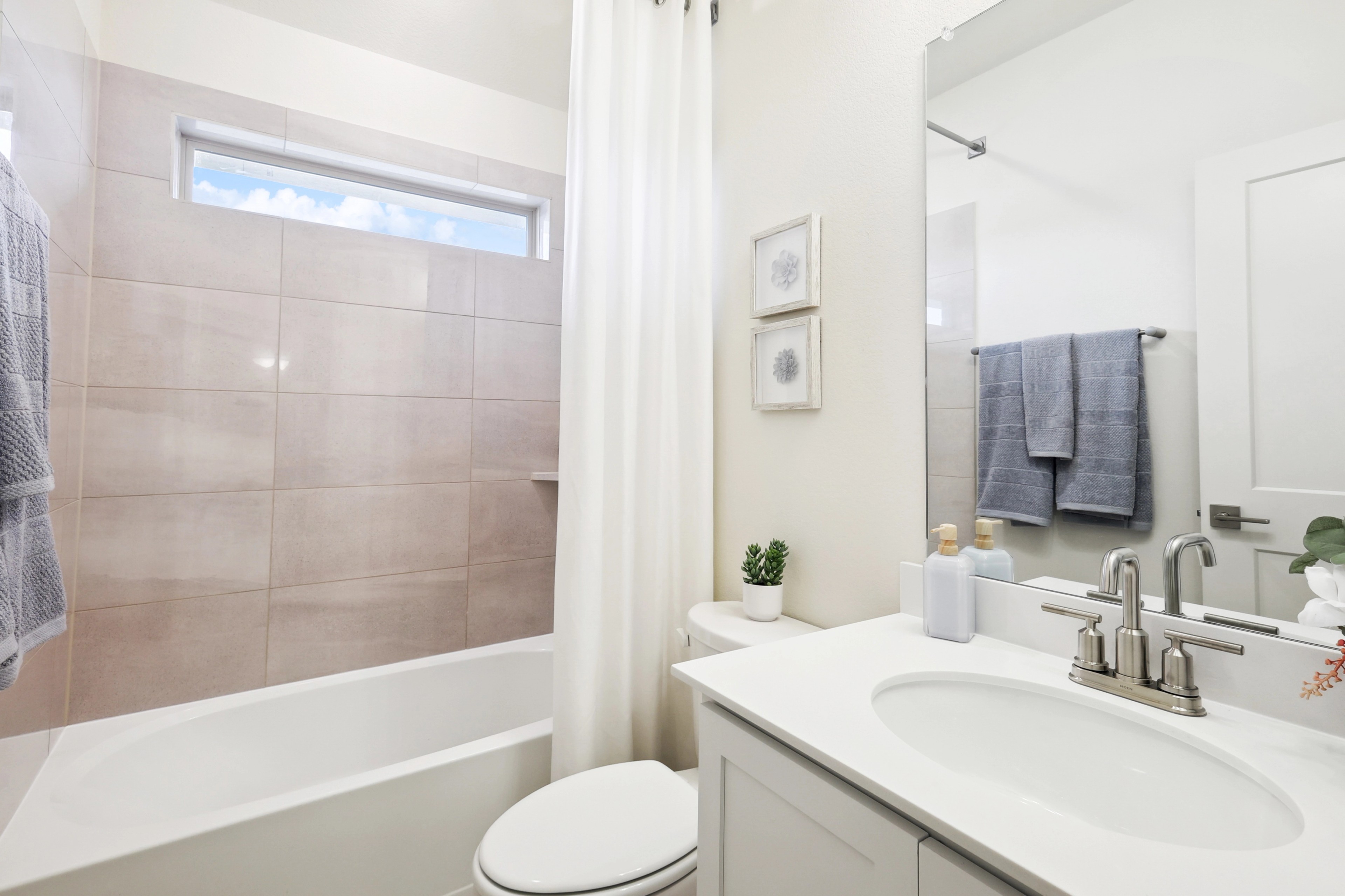 Modern bathroom with bathtub, beige tiles, minimalist decor, and window light in The Oaks community.