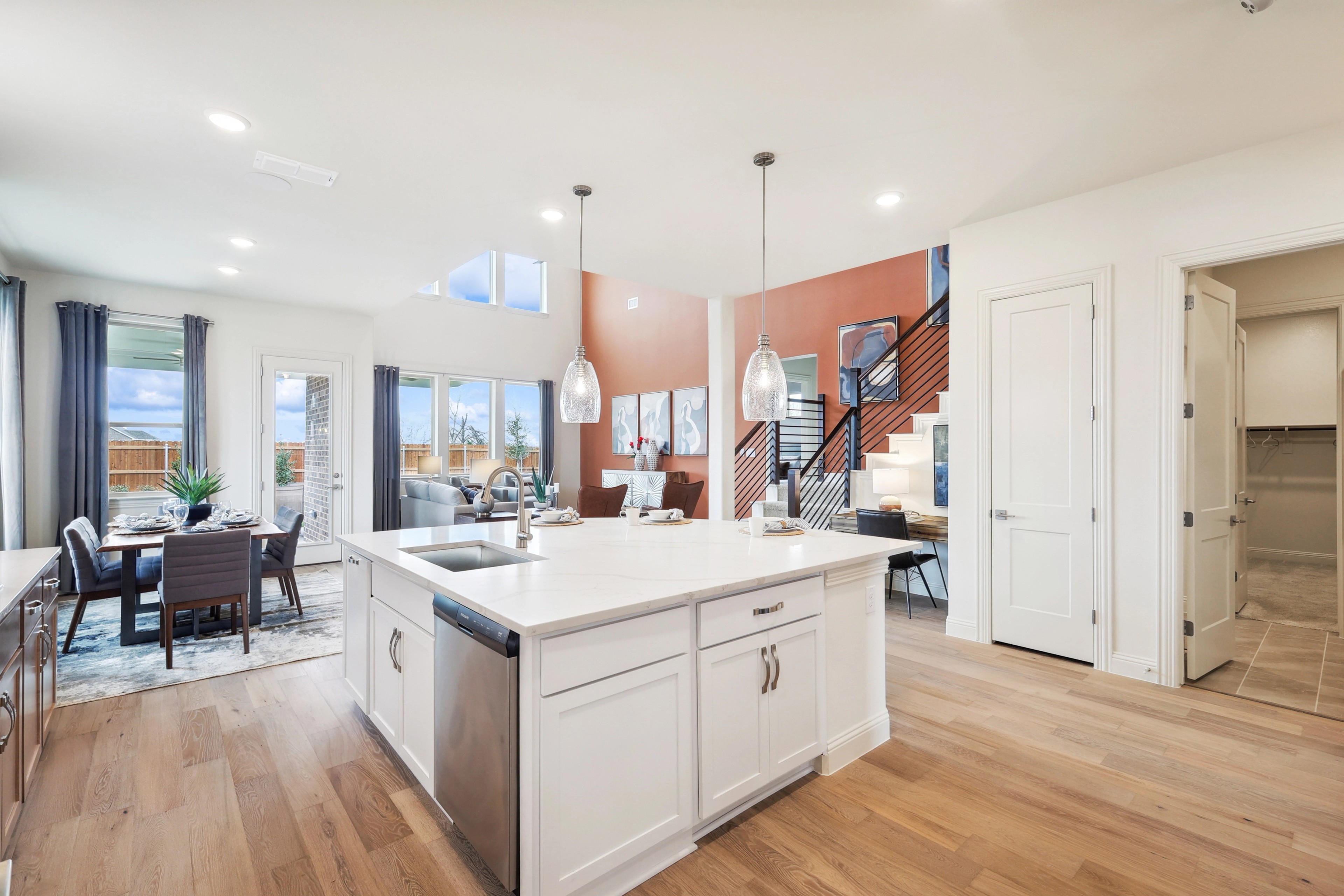 Modern kitchen with white island, pendant lights, open layout, wood floors in The Oaks community. Bright and spacious.