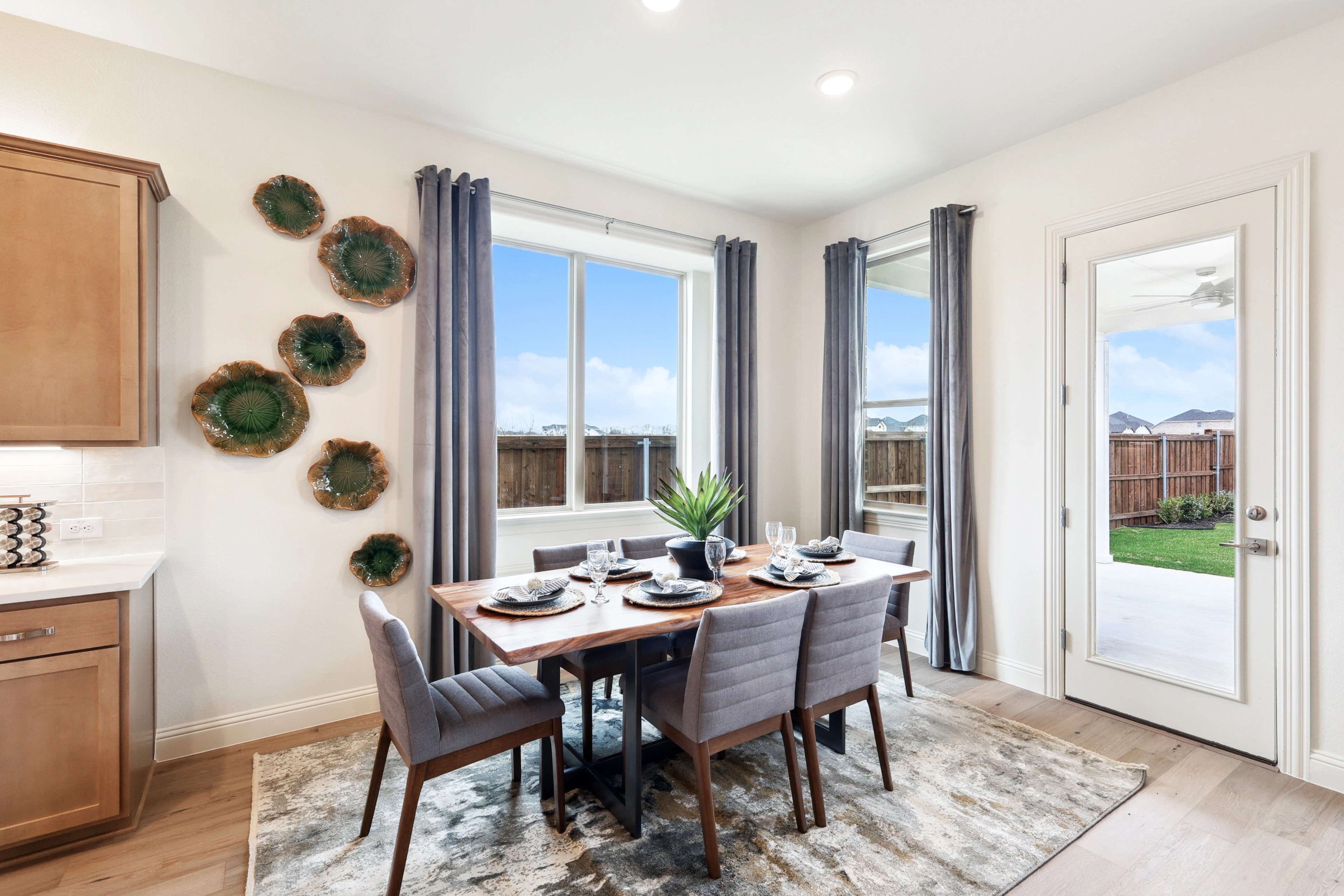 Elegant dining room features a wooden table, gray chairs, large windows, and wall art in The Oaks community.