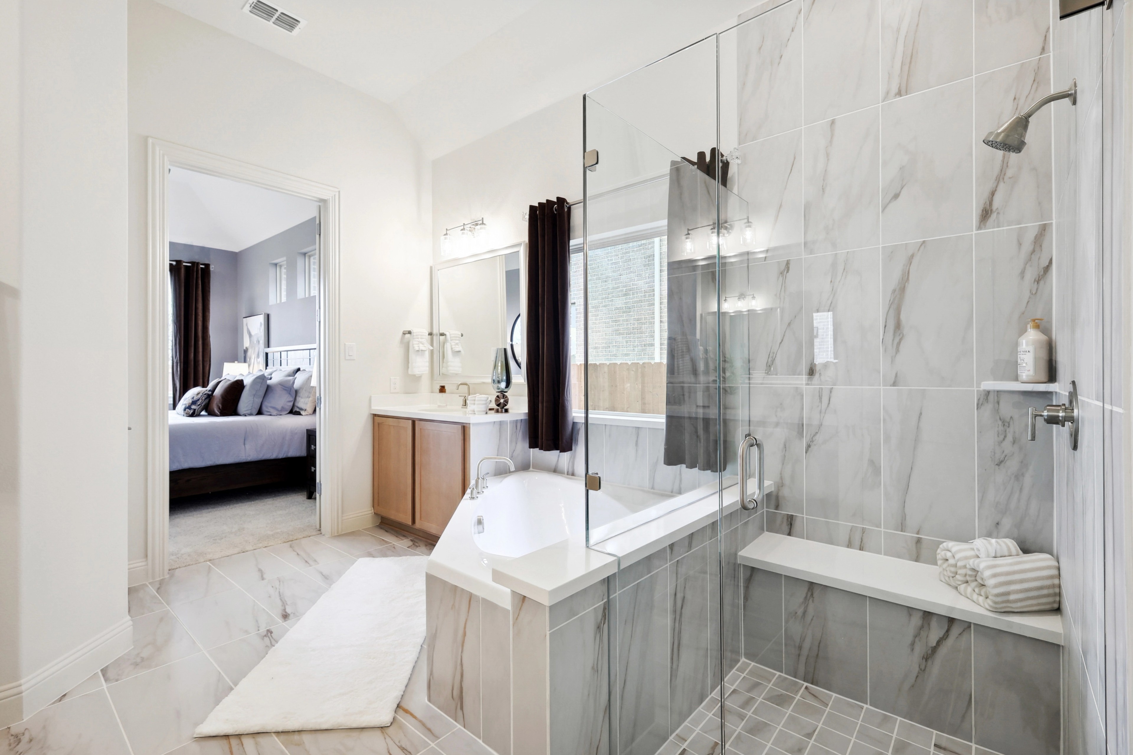 Luxurious master bathroom featuring a glass shower, marble tiles, and freestanding tub in The Oaks community.