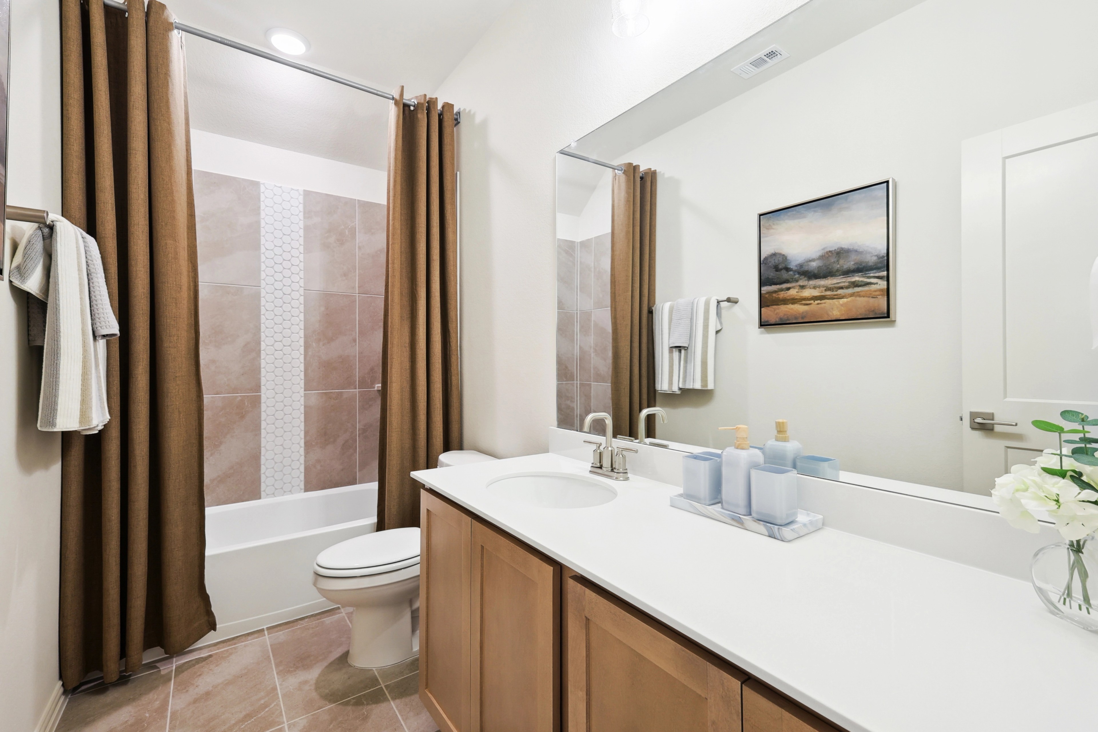 Modern bathroom with wood vanity, art piece, and tiled shower in The Oaks community.