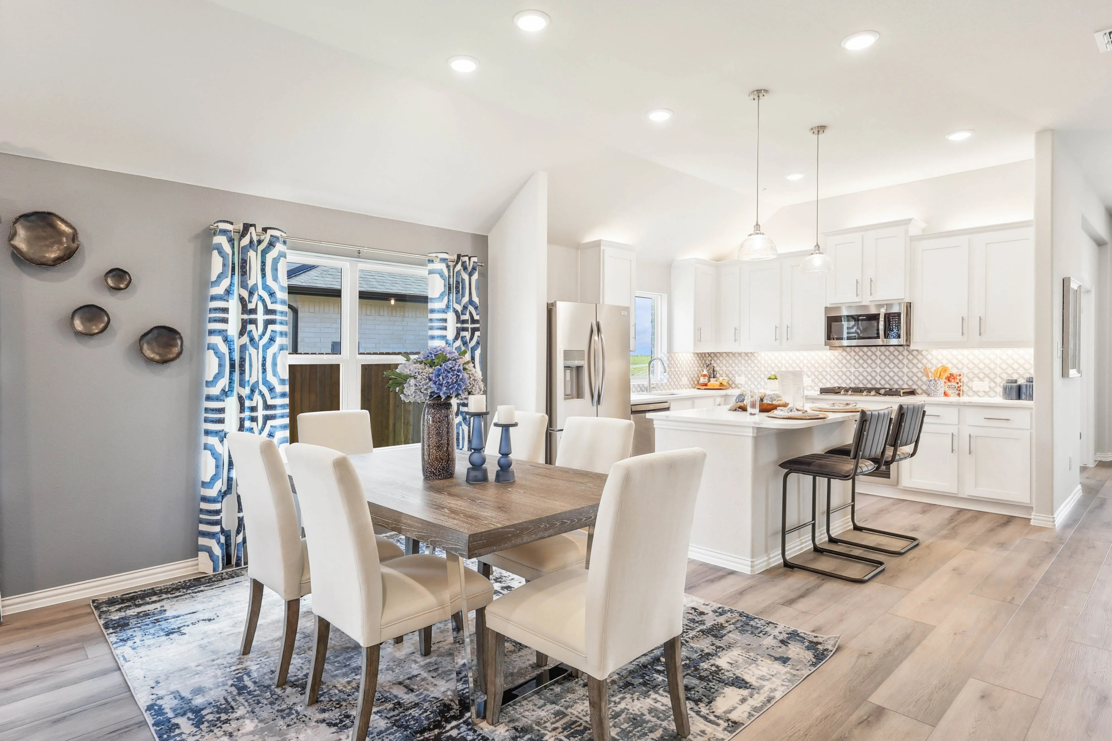 Modern dining area and kitchen with white cabinets, island, wood flooring, Texas home.